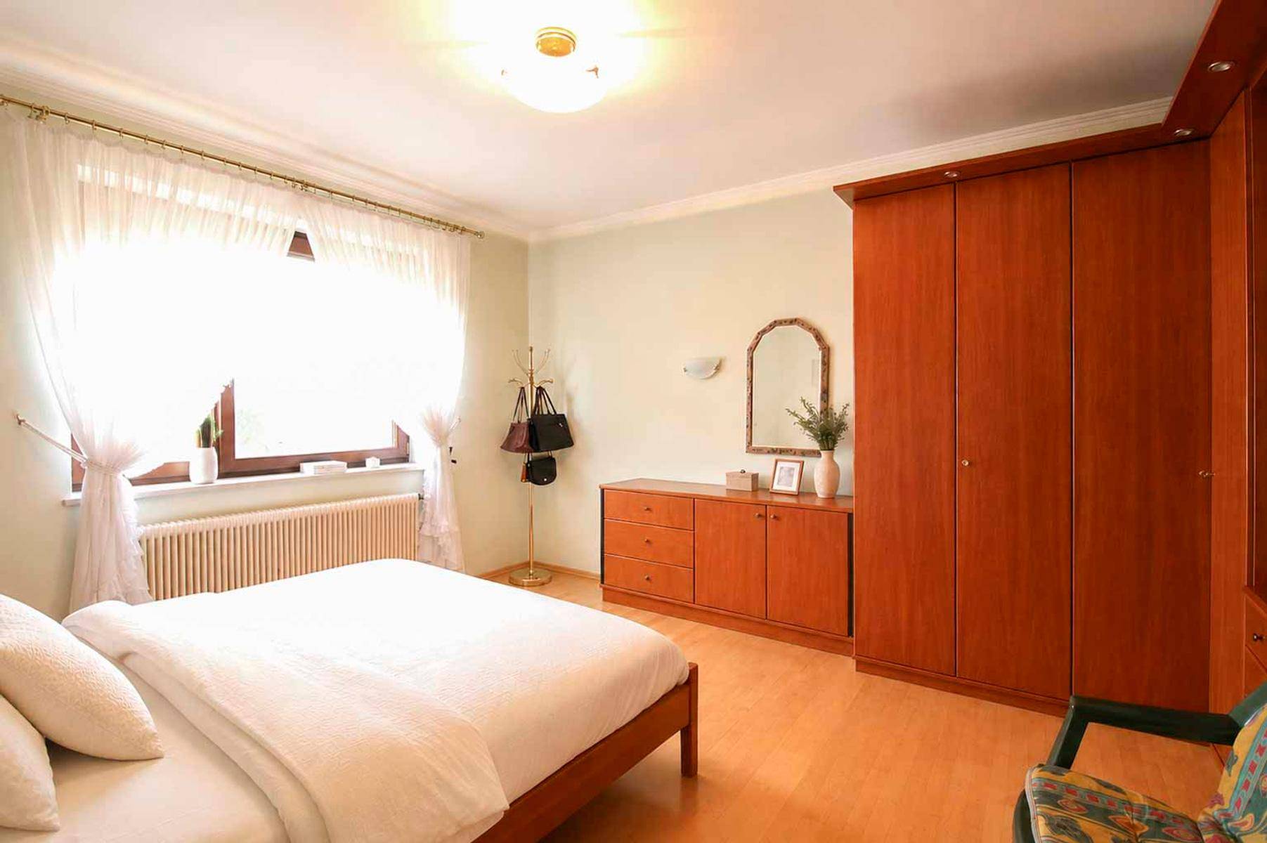 Helles Schlafzimmer mit Holzboden, großem Kleiderschrank und Fenster mit Vorhängen.