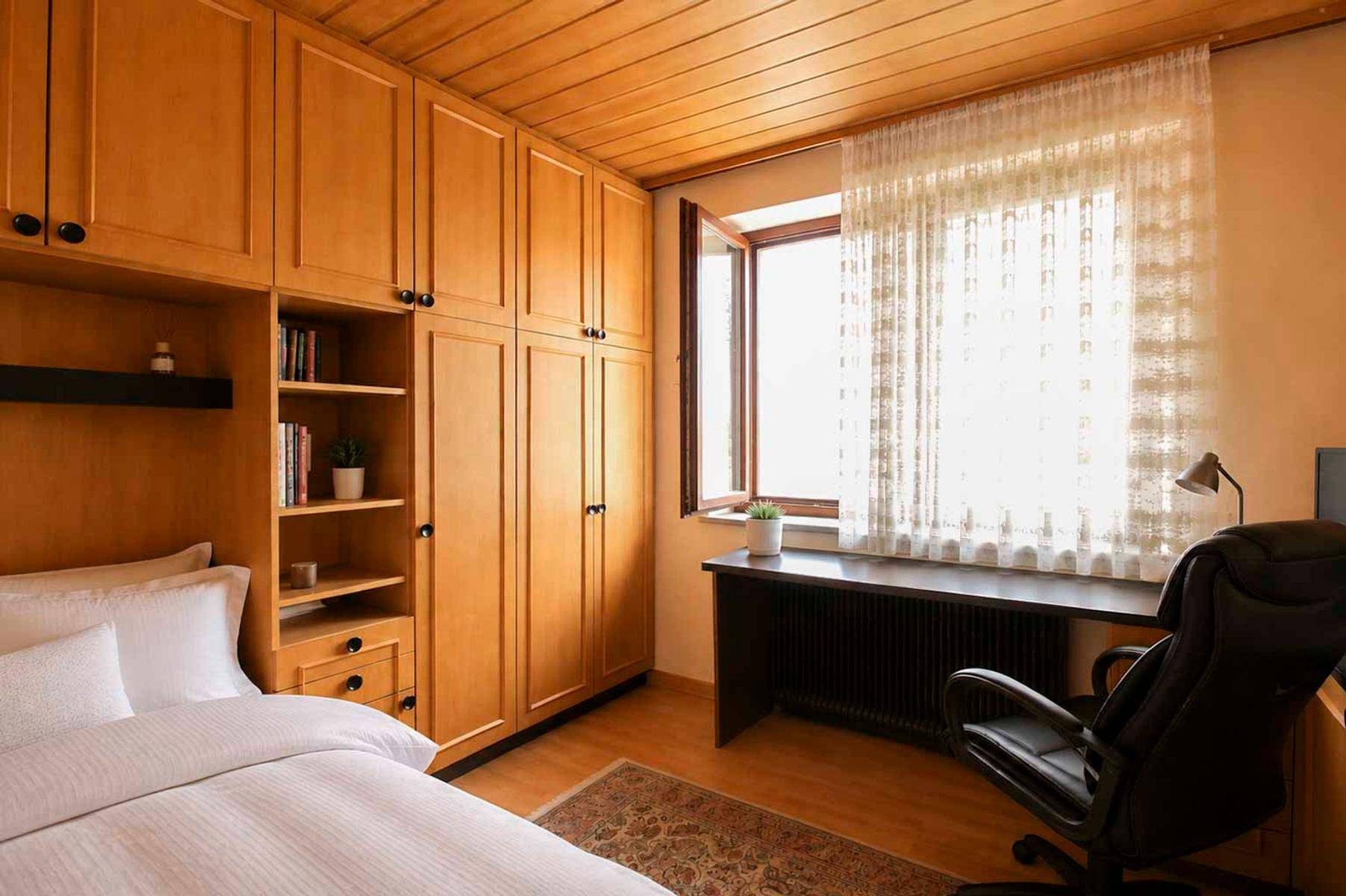 Schlafzimmer mit Einbauschränken, Holzboden und Schreibtisch am Fenster.