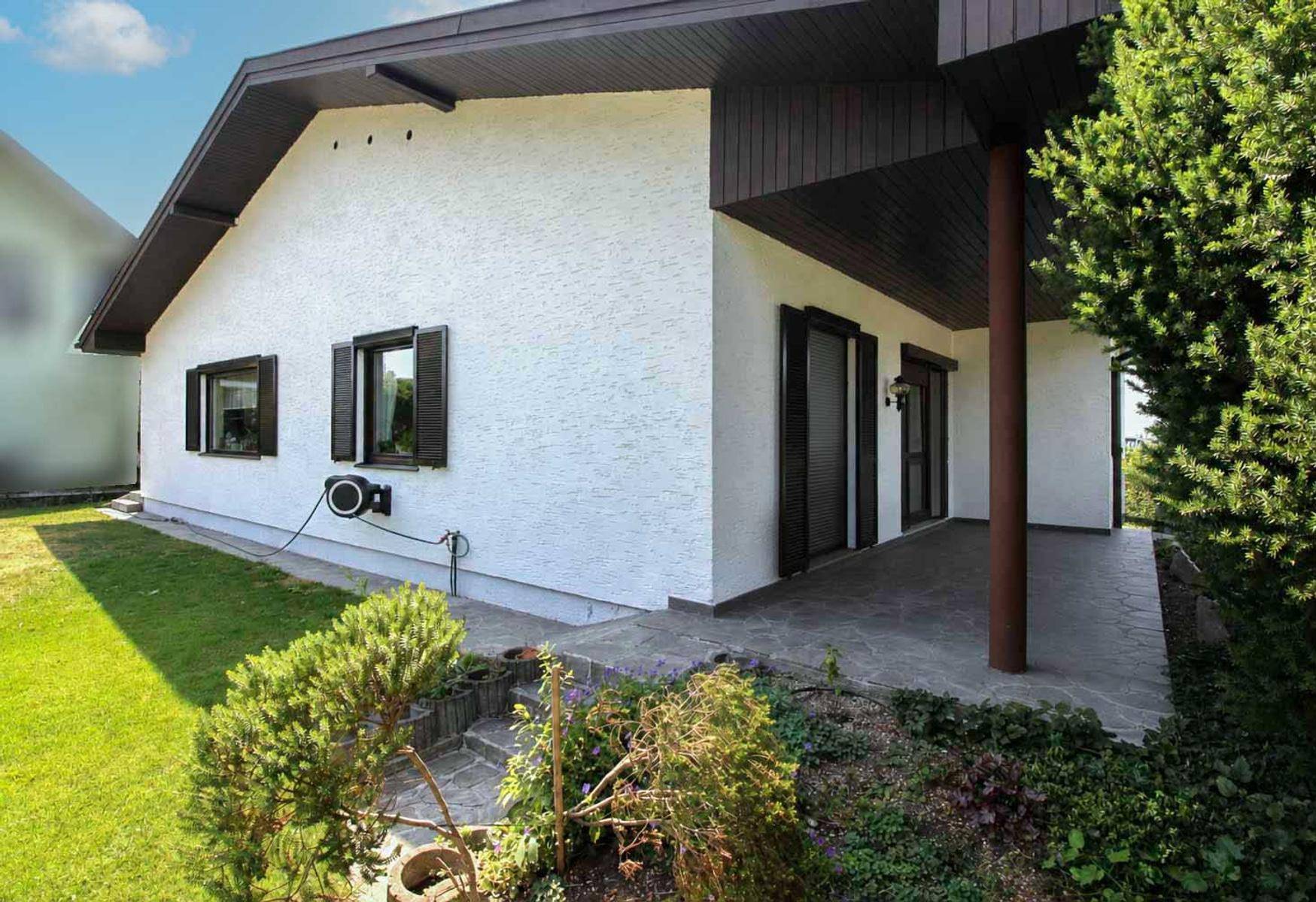 Überdachte Terrasse am Haus mit Steinfliesen und Zugang zum Gartenbereich.