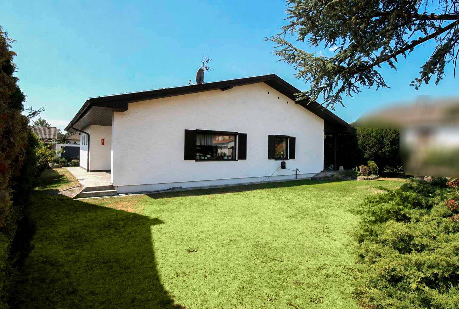Rückseite des Einfamilienhauses mit großem Rasen und grüner Bepflanzung unter blauem Himmel.