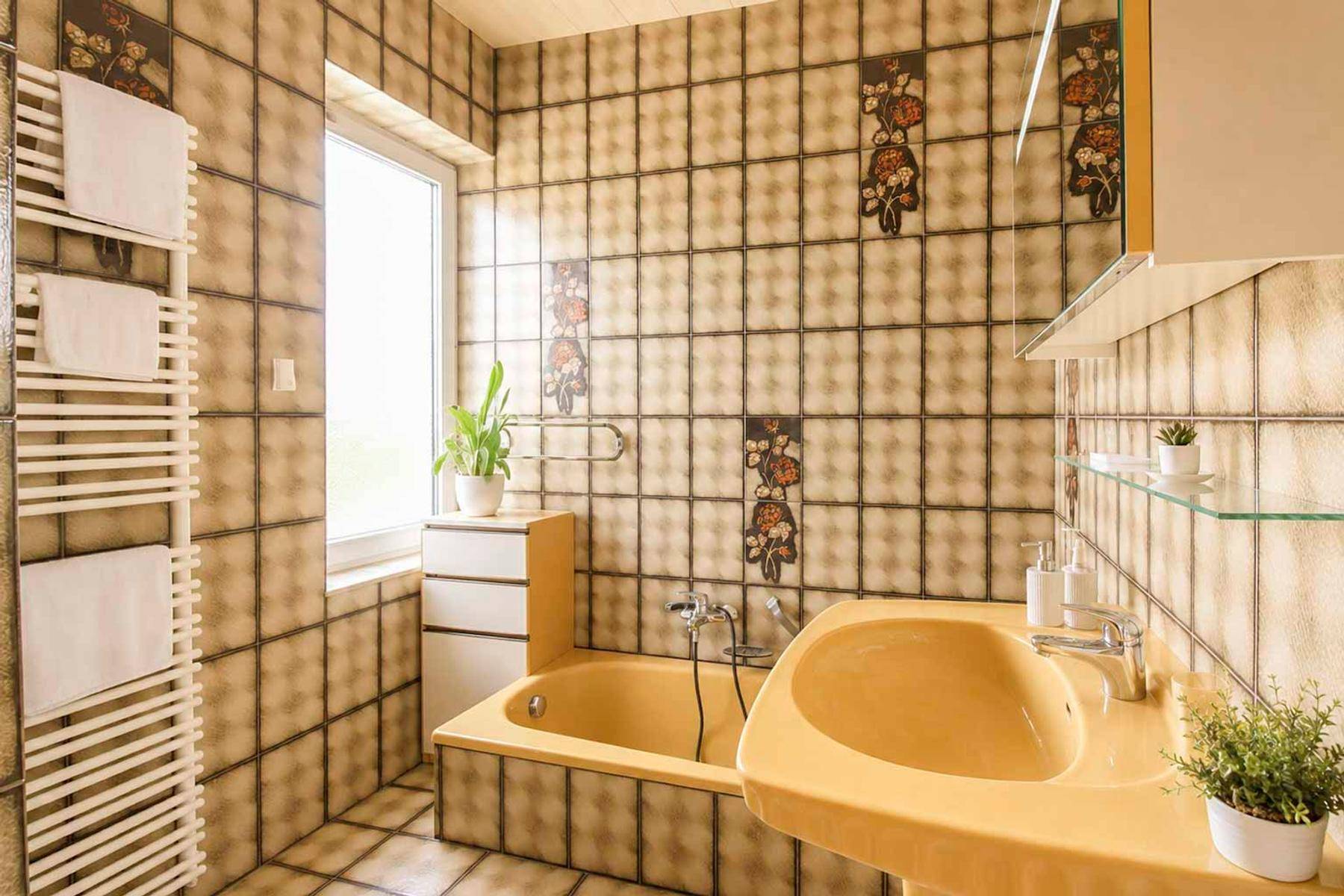 Badezimmer im 80er-Jahre-Stil mit gelber Badewanne, Waschbecken und Fliesen.