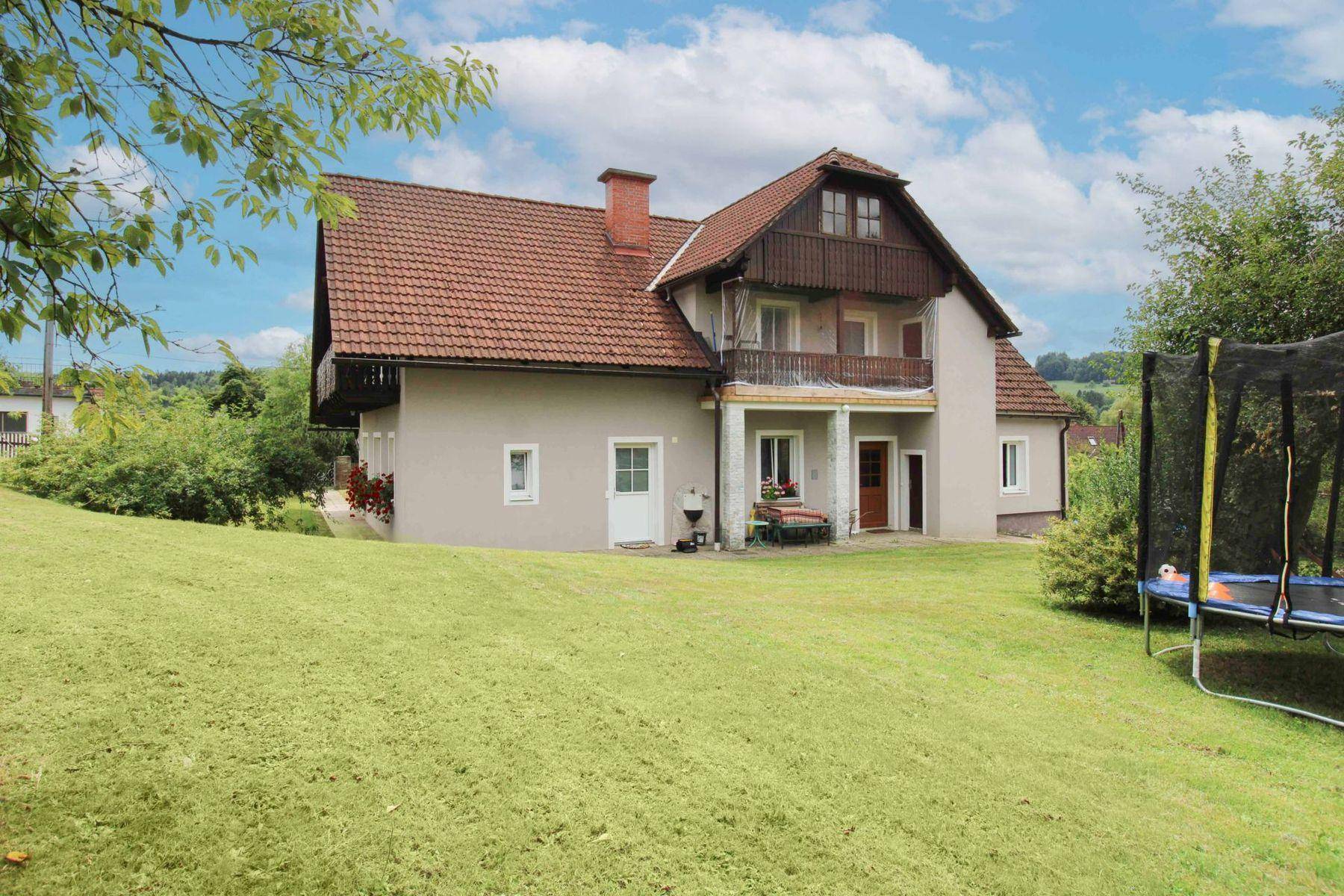 Wohnhaus mit weitläufigem Rasengarten und Trampolin, umgeben von grüner Natur.