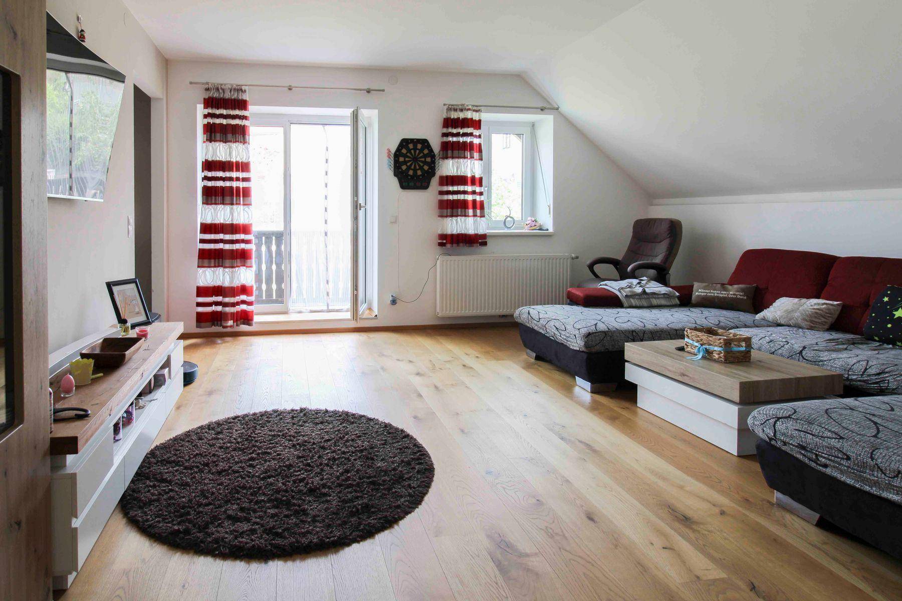Geräumiges Wohnzimmer im Dachgeschoss mit Holzboden, bequemer Sofalandschaft und Balkonzugang.