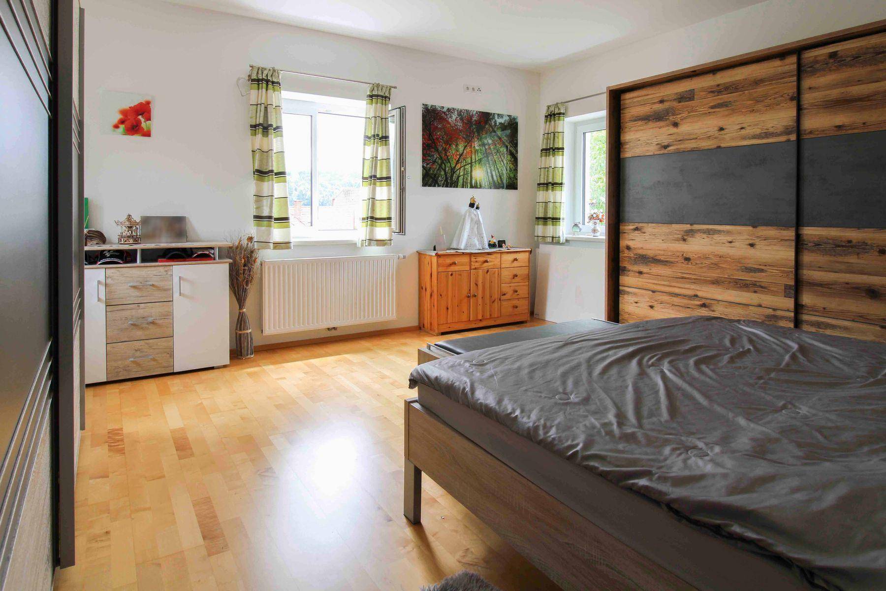 Helles Schlafzimmer mit Holzboden, großem Schiebetürenschrank und zwei Fenstern.