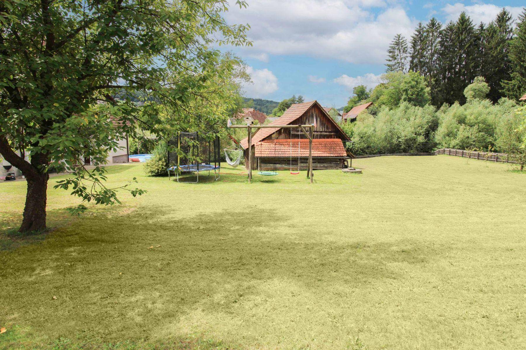 Großer Rasengarten mit Schaukel und Trampolin, umgeben von Bäumen und einem Holzgebäude.