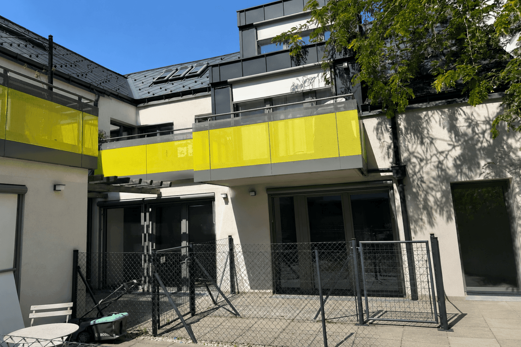 Moderne Gebäudefassade mit gelben Balkonen und großen Fensterfronten, umgeben von Grünflächen.