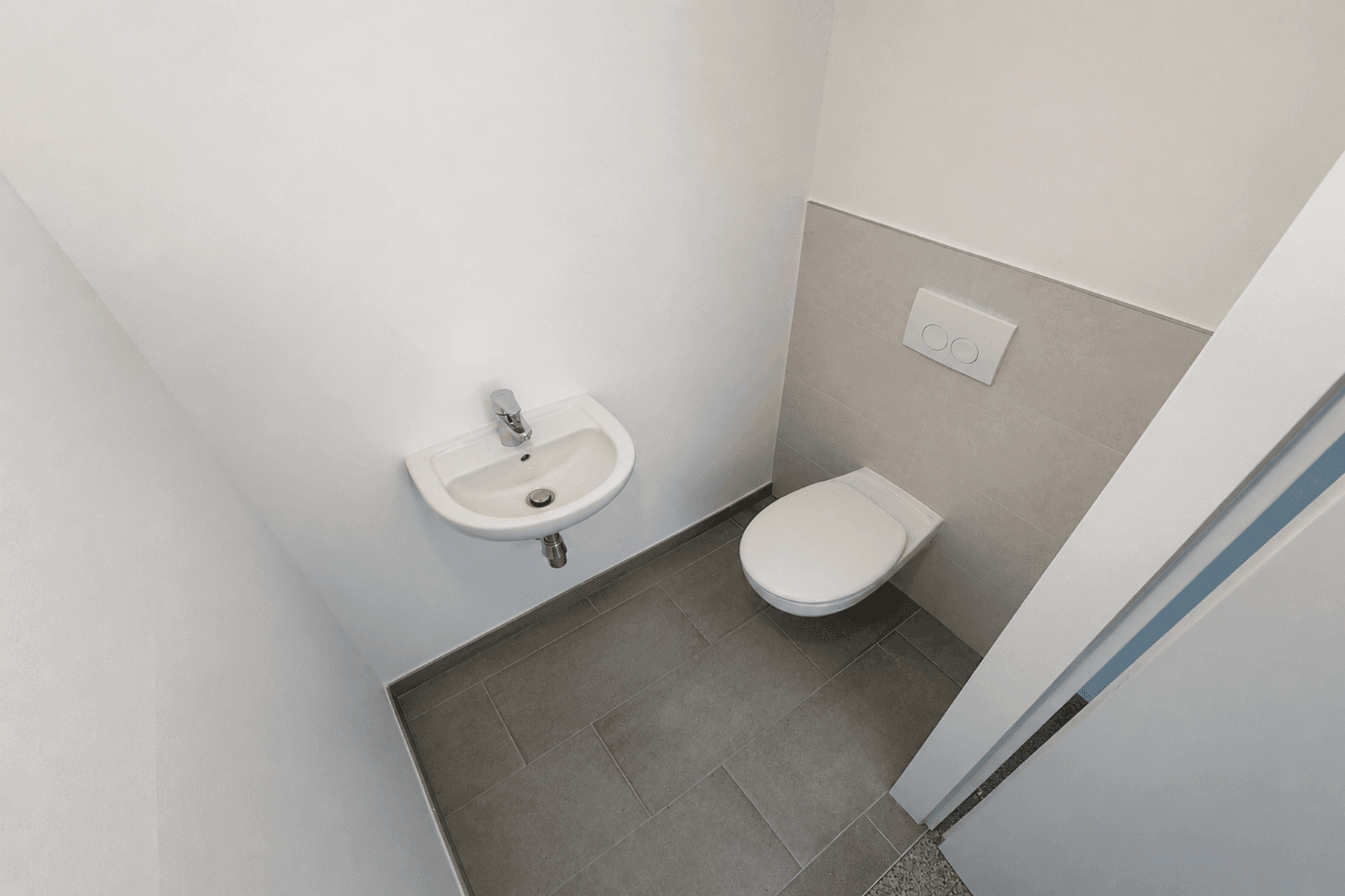 Modernes Gäste-WC mit wandhängender Toilette und kleinem Waschbecken, gefliest in Grau- und Beigetönen.