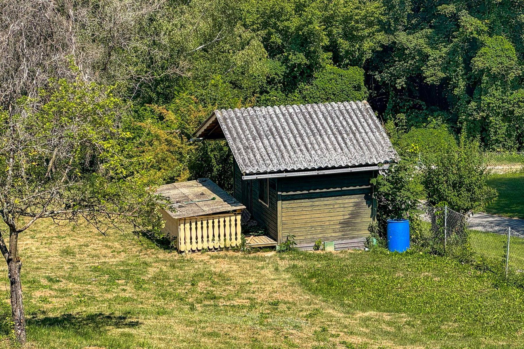Idyllischer Gartenabschnitt mit einem kleinen Holzschuppen und üppiger Vegetation im Hintergrund.