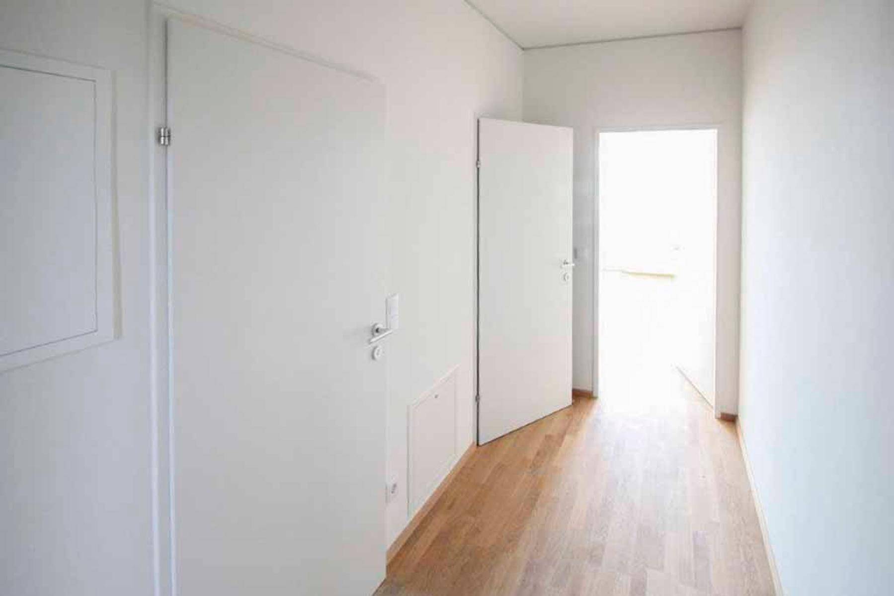 Heller Flur mit Holzboden und weißen Türen, der zu weiteren, lichtdurchfluteten Räumen führt.