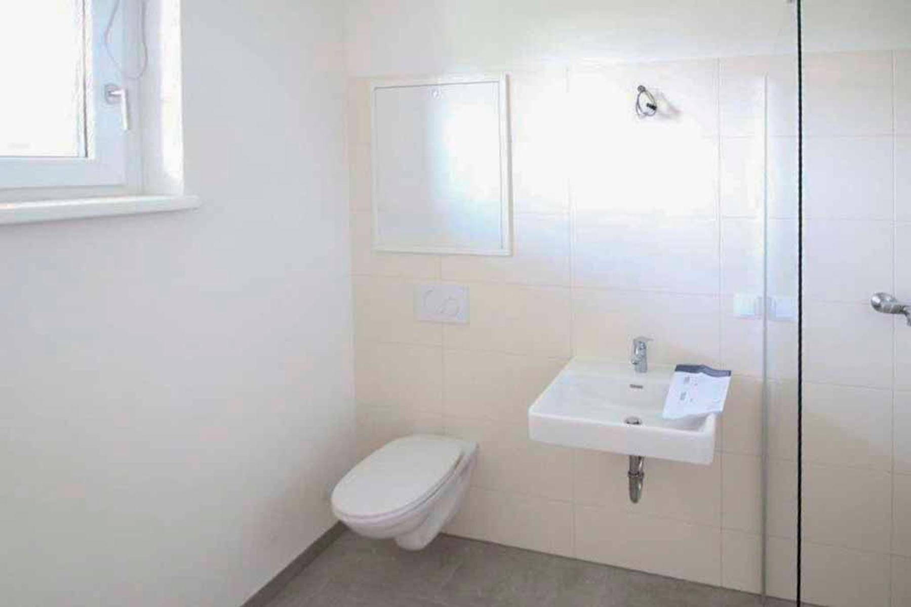 Modernes Gäste-WC mit wandhängender Toilette, kleinem Waschbecken und Fenster.