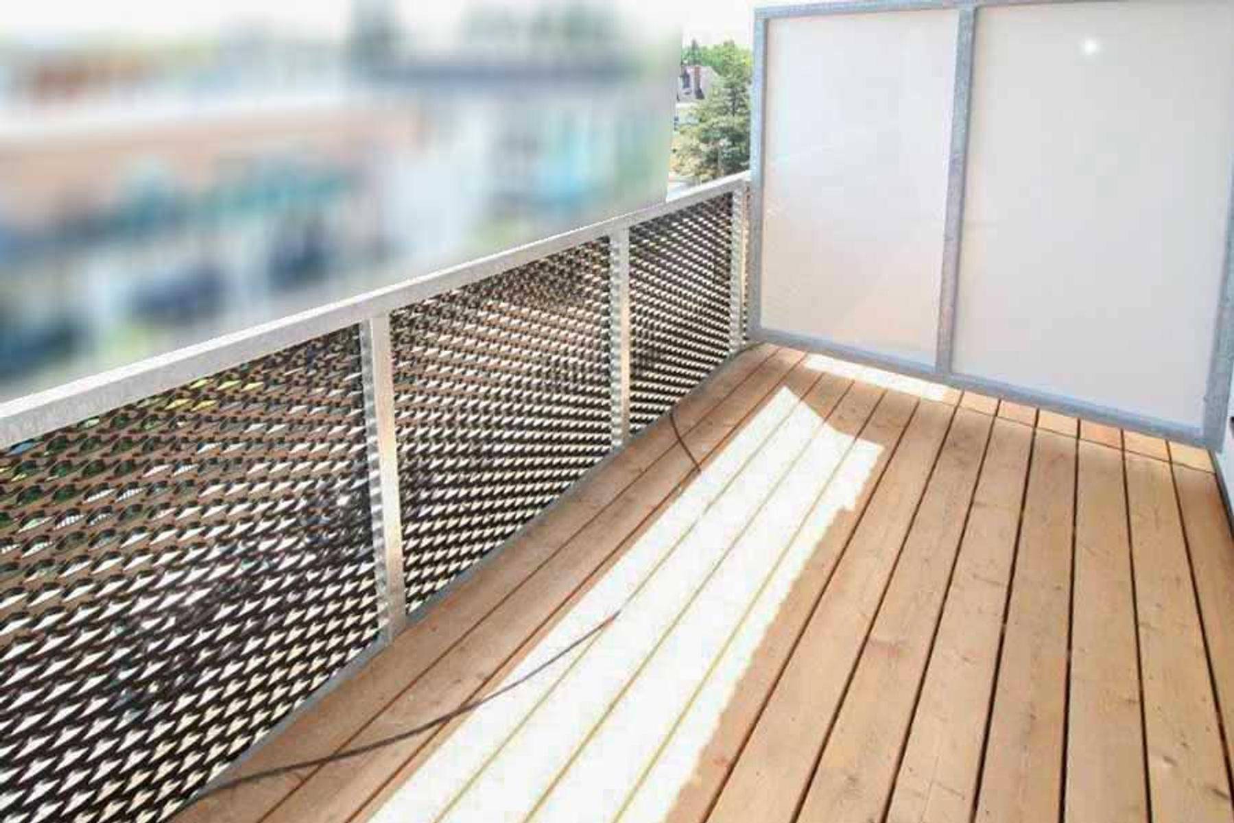 Sonniger Balkon mit Holzboden und Metallgeländer, bietet Platz zum Entspannen.