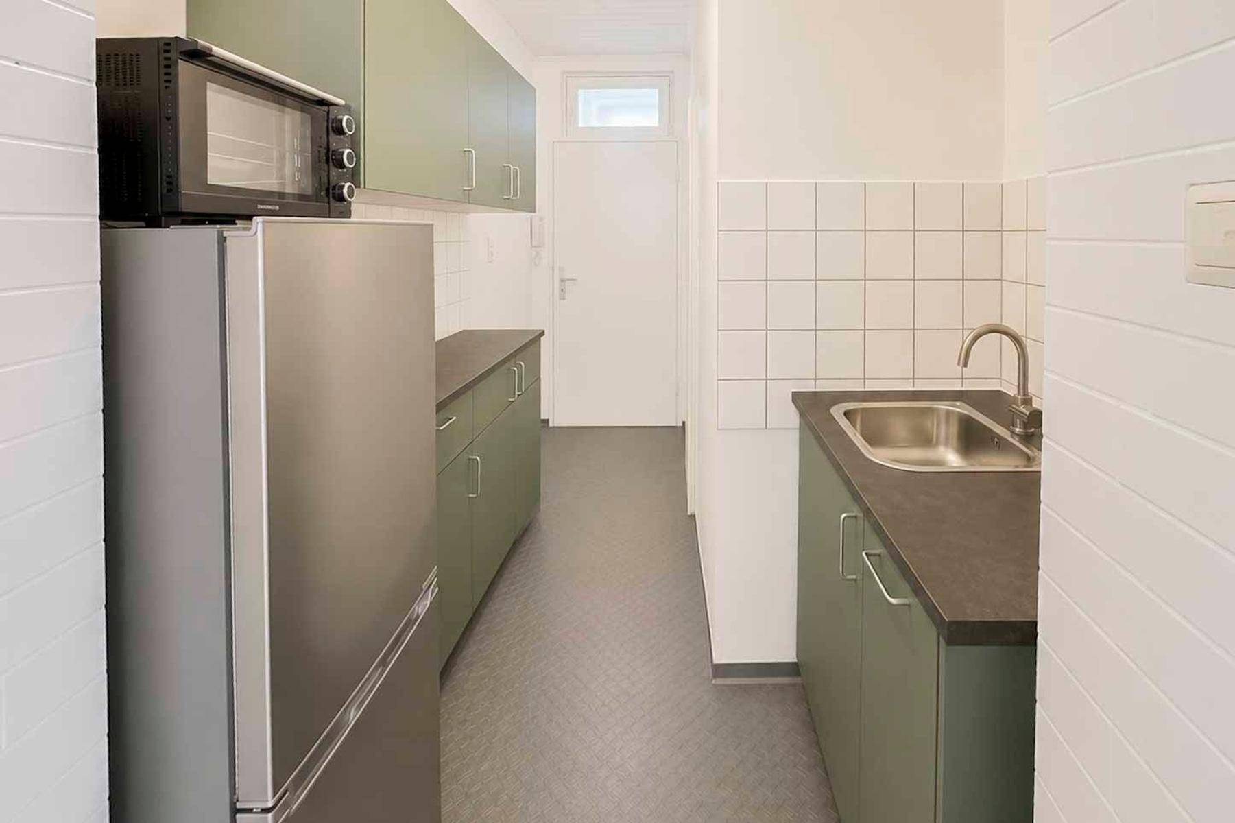 Schmale Küche mit grünen Schränken, Kühlschrank und Mikrowelle.