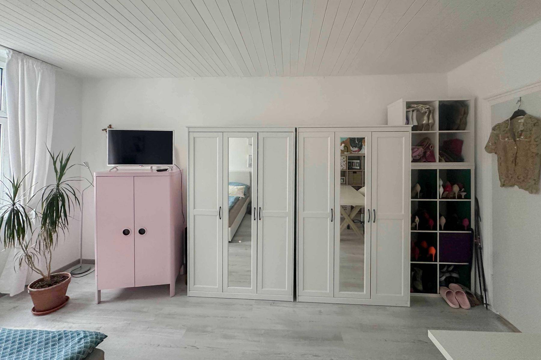 Schlafzimmer mit weißen Kleiderschränken, Spiegeln und einem rosa Schrank.
