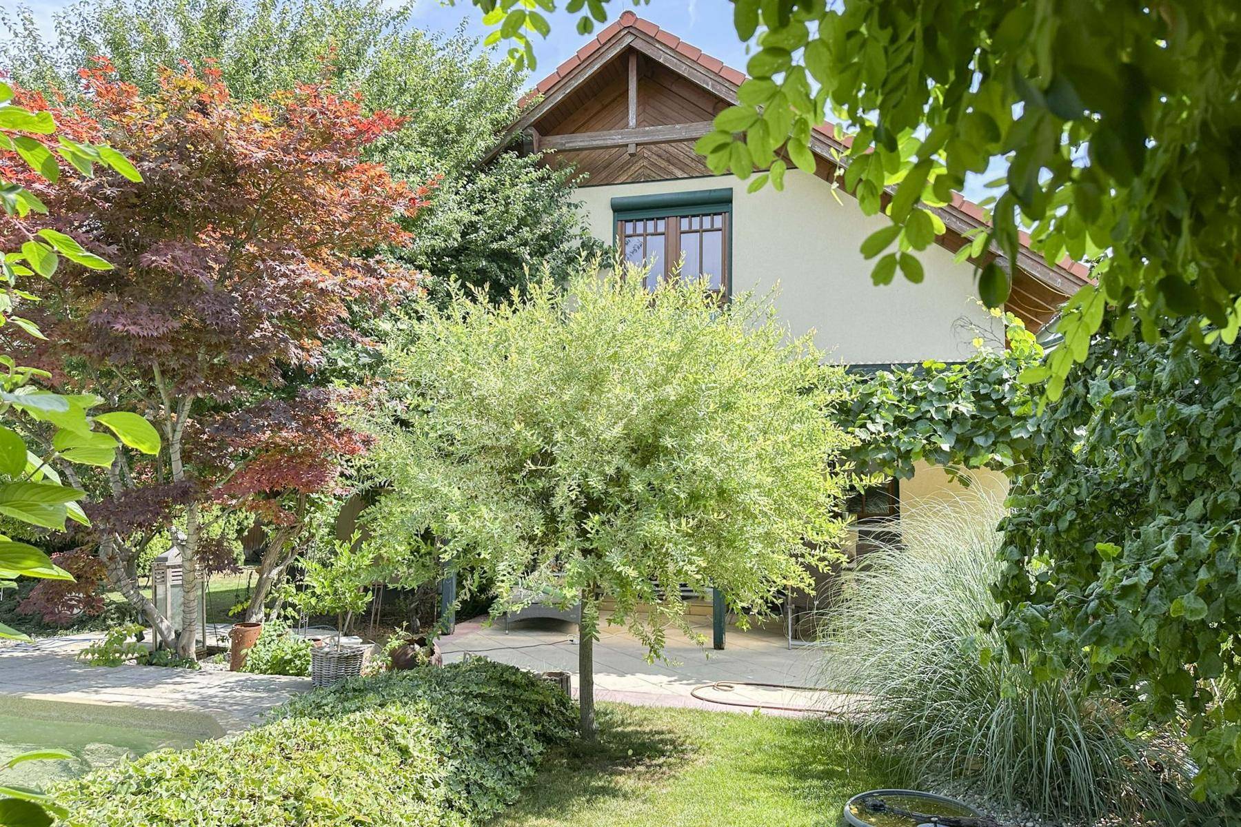 Rückansicht des Hauses mit Terrasse und üppigem Garten, umgeben von Bäumen.