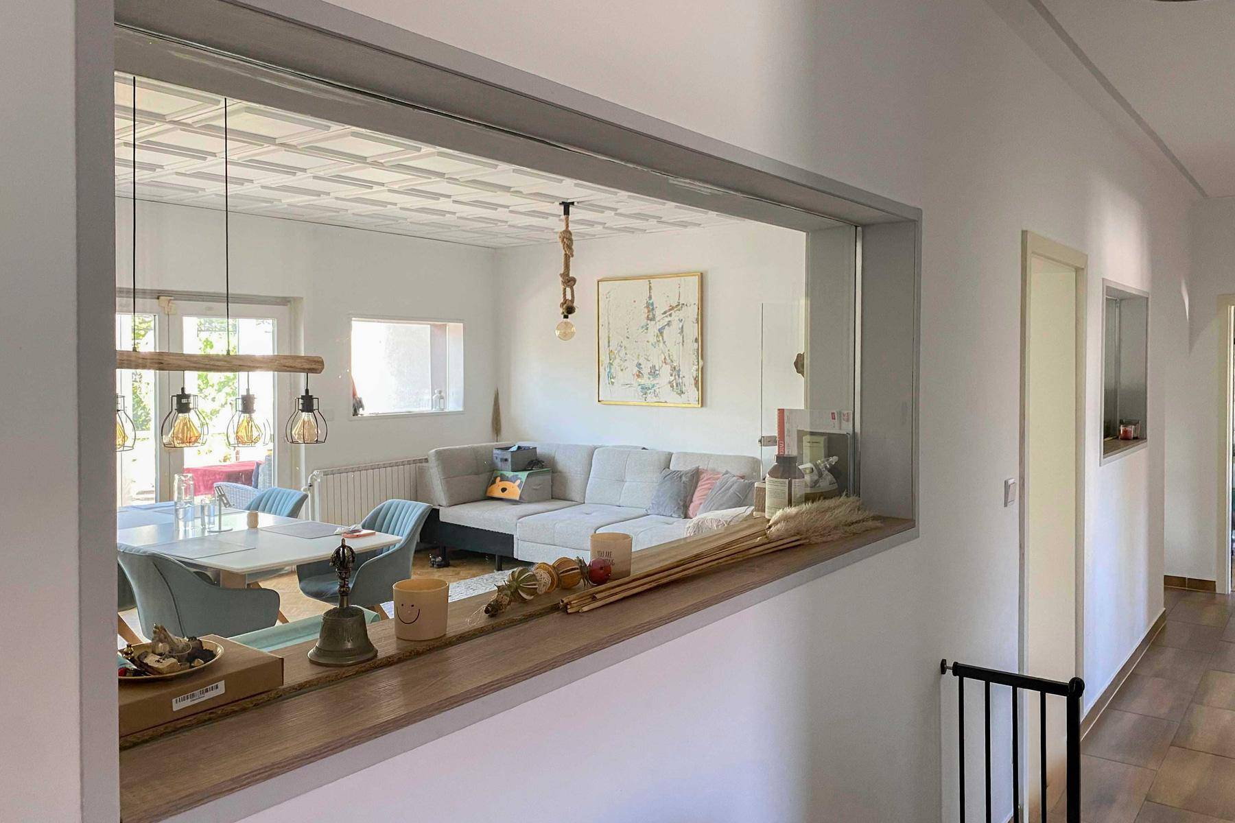 Blick vom Flur in den offenen Wohn-Essbereich mit Sofa, Esstisch und dekorativer Decke.