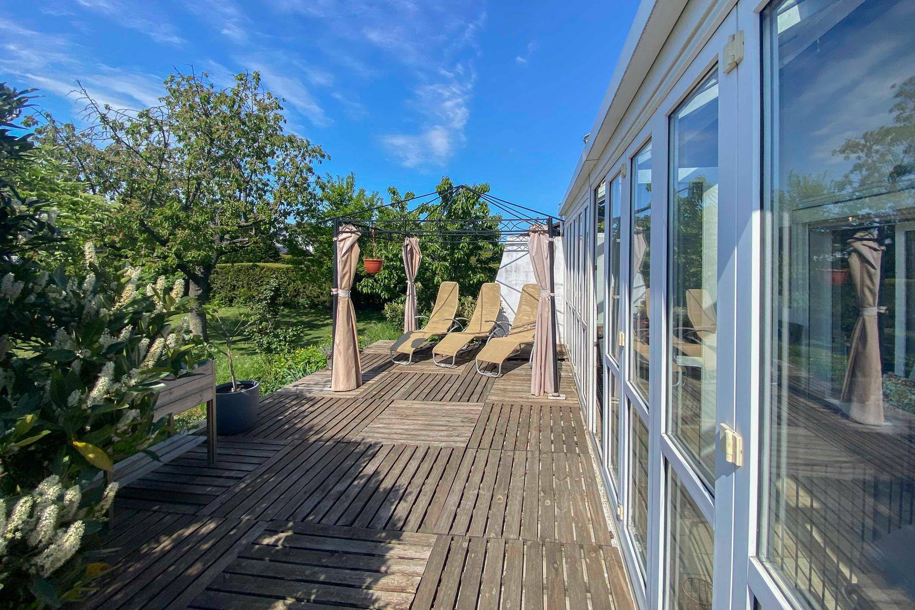Sonnige Holzterrasse mit Liegestühlen und Pavillon, angrenzend an den Wintergarten.