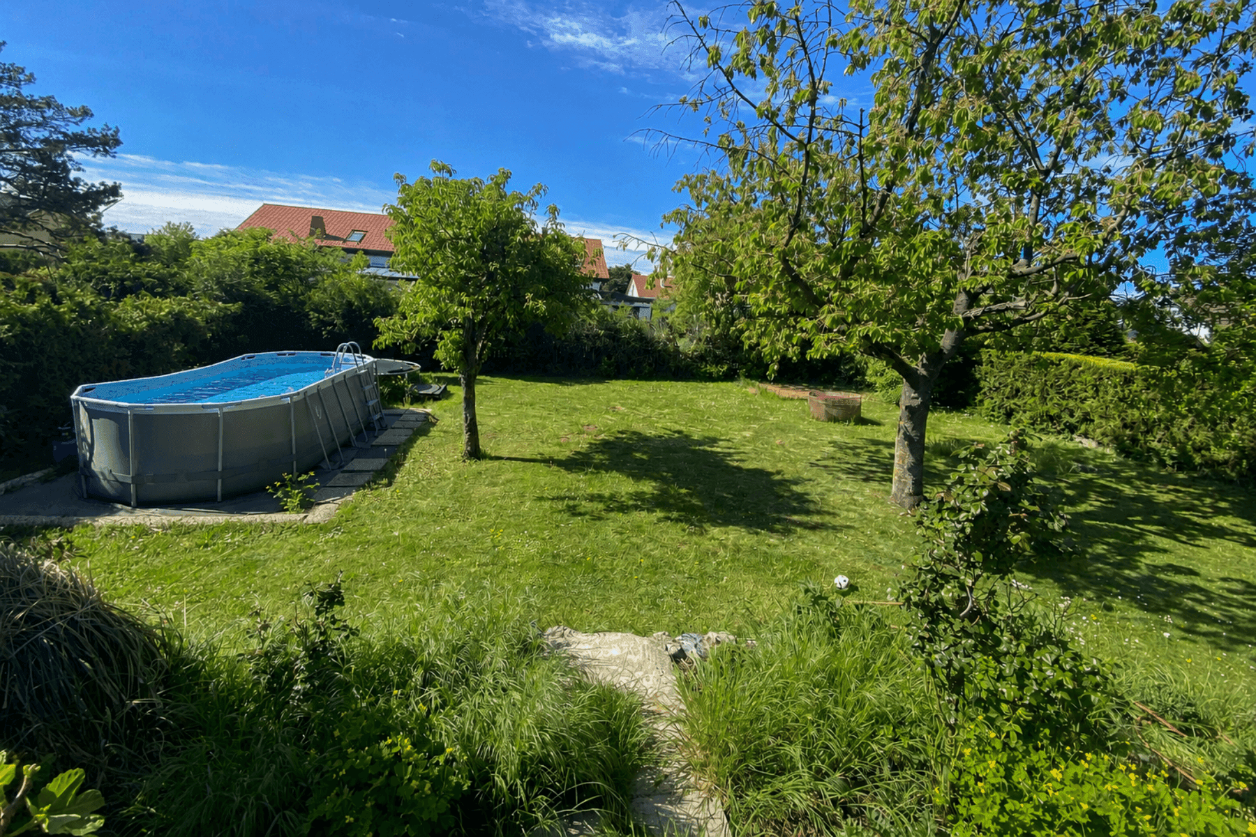 Weitläufiger Garten mit großem Rasenbereich, Bäumen und einem Aufstellpool.