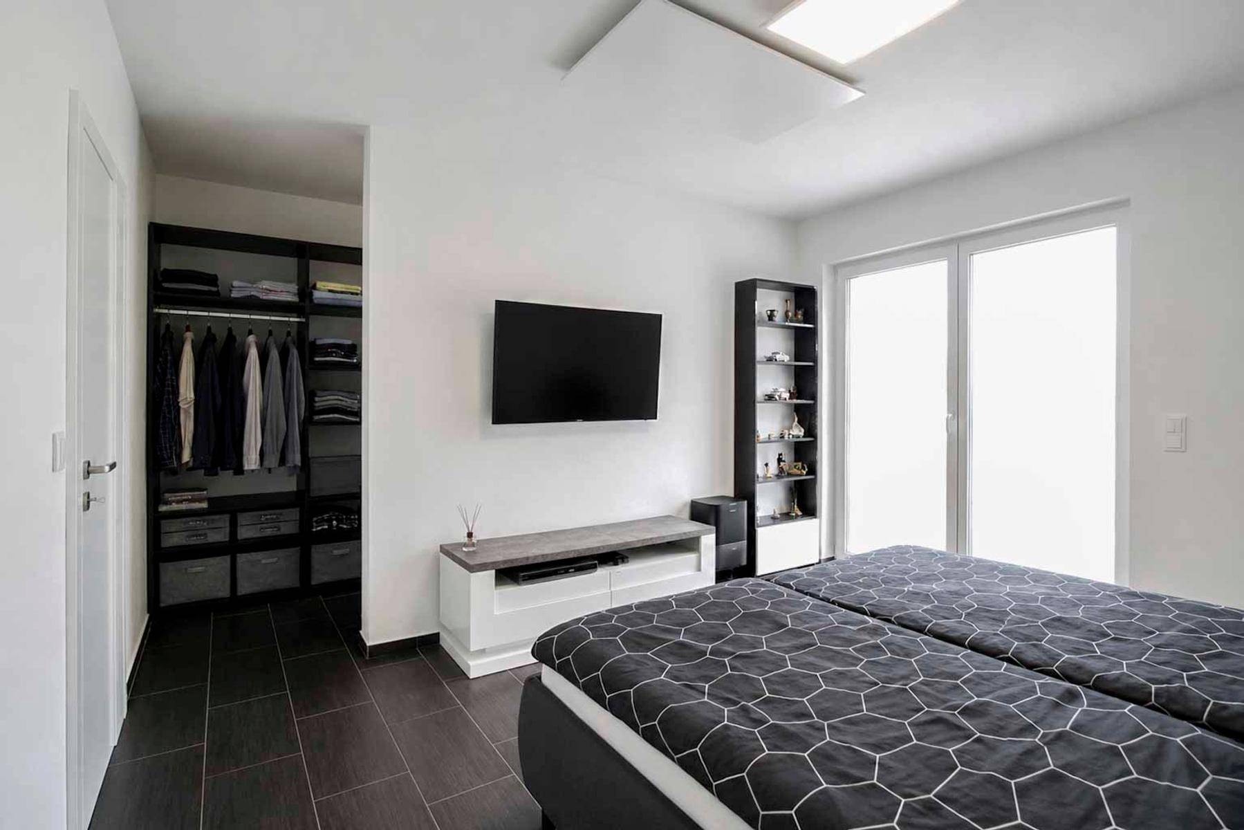 Schlafzimmer mit Doppelbett, Wandfernseher und offenem Zugang zu einem begehbaren Kleiderschrank.