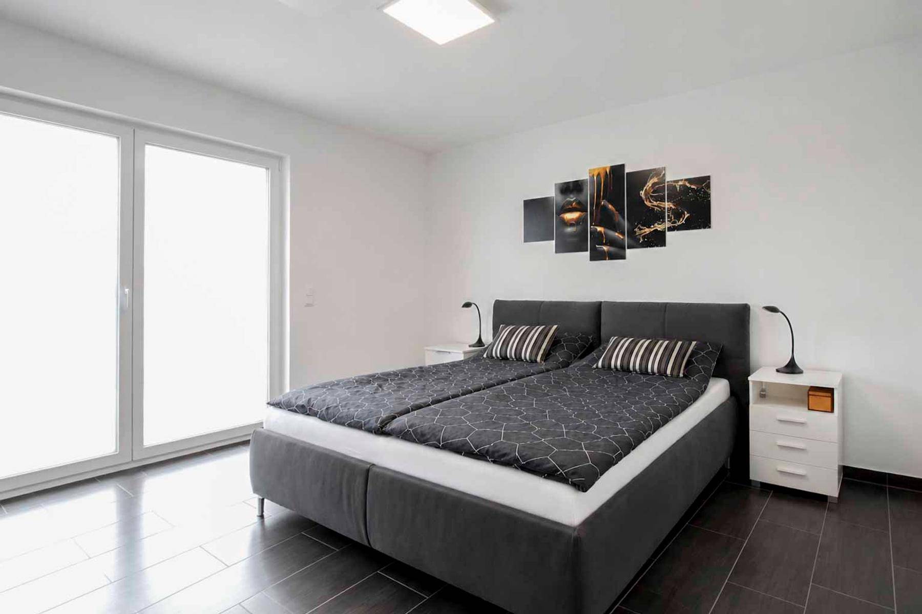 Schlafzimmer mit großem Doppelbett, dunklen Fliesen und Zugang zu einem Balkon oder Terrasse.