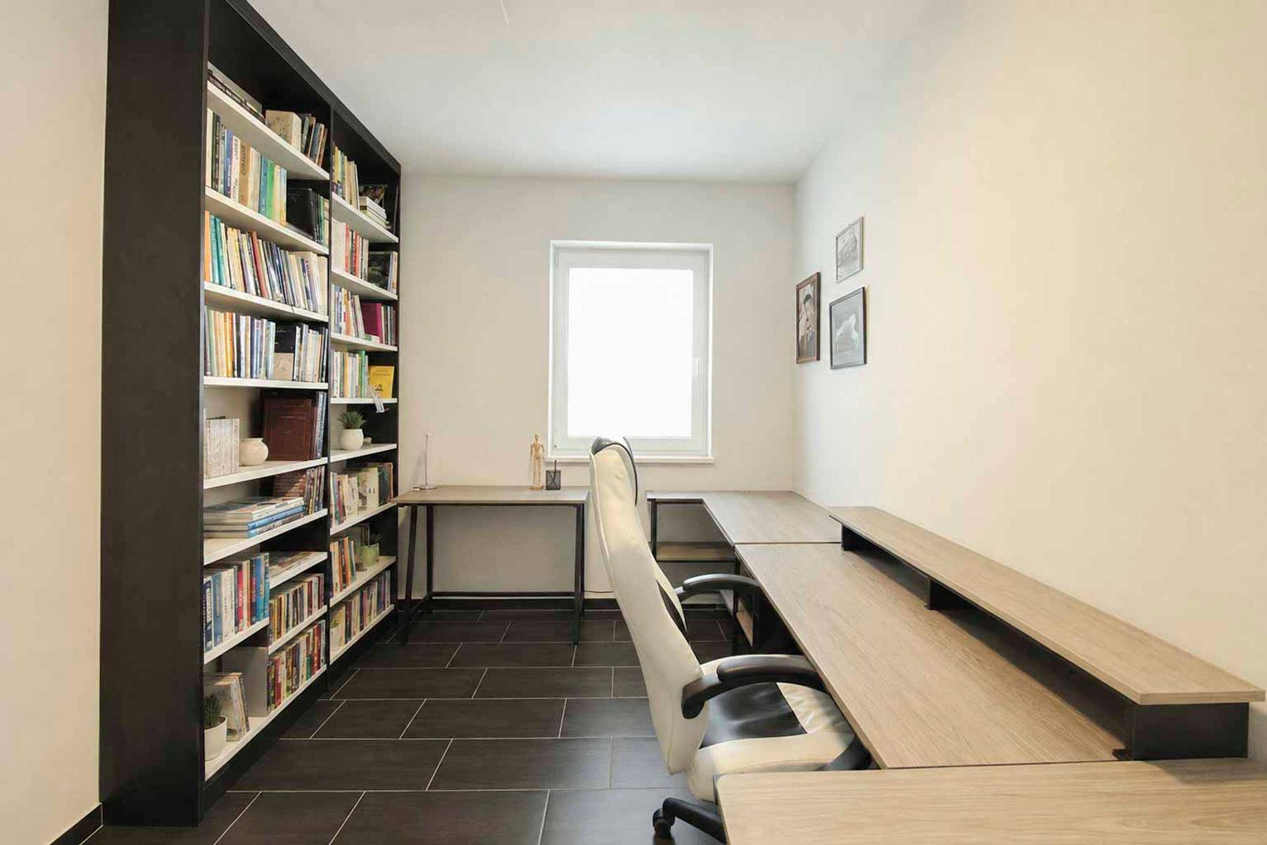 Helles Arbeitszimmer mit großem Bücherregal, Schreibtischen und Fenster für Tageslicht.
