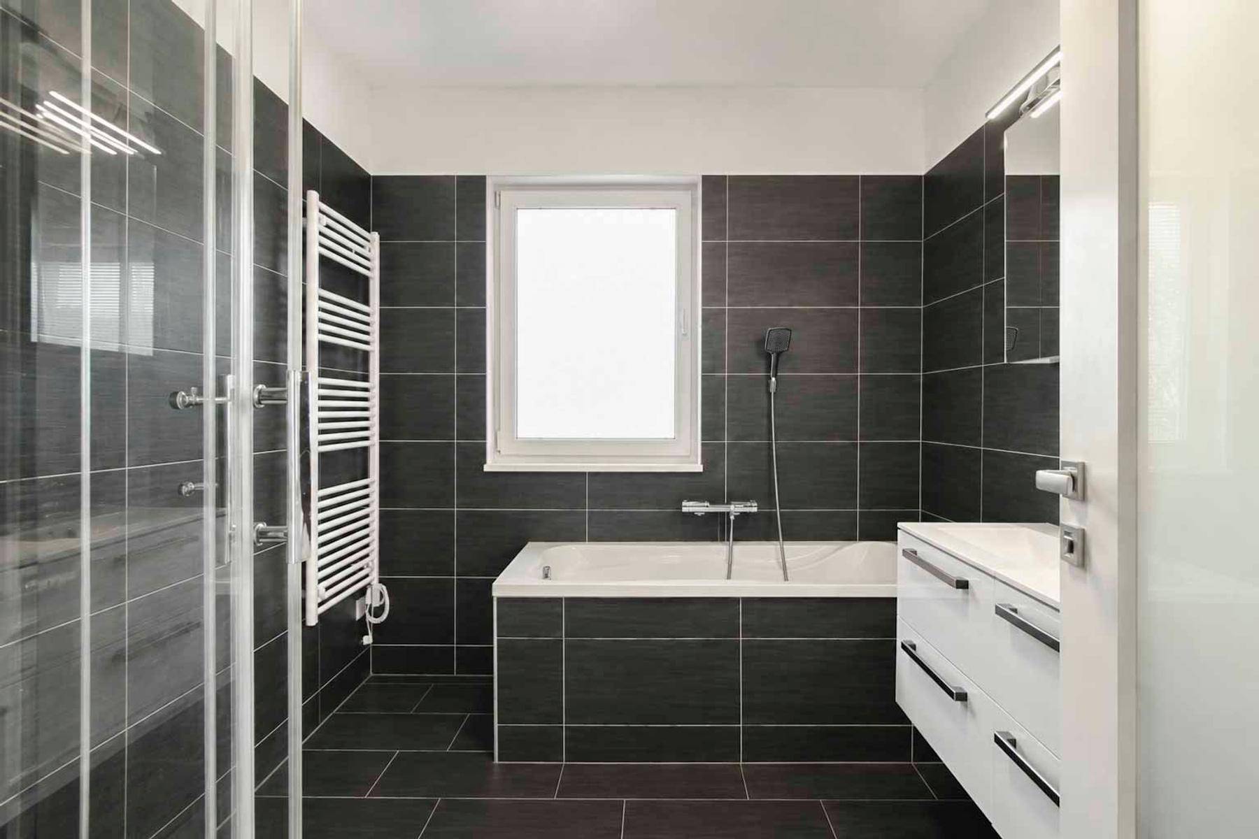 Modernes Badezimmer mit dunklen Fliesen, Badewanne, Dusche und beheiztem Handtuchhalter.