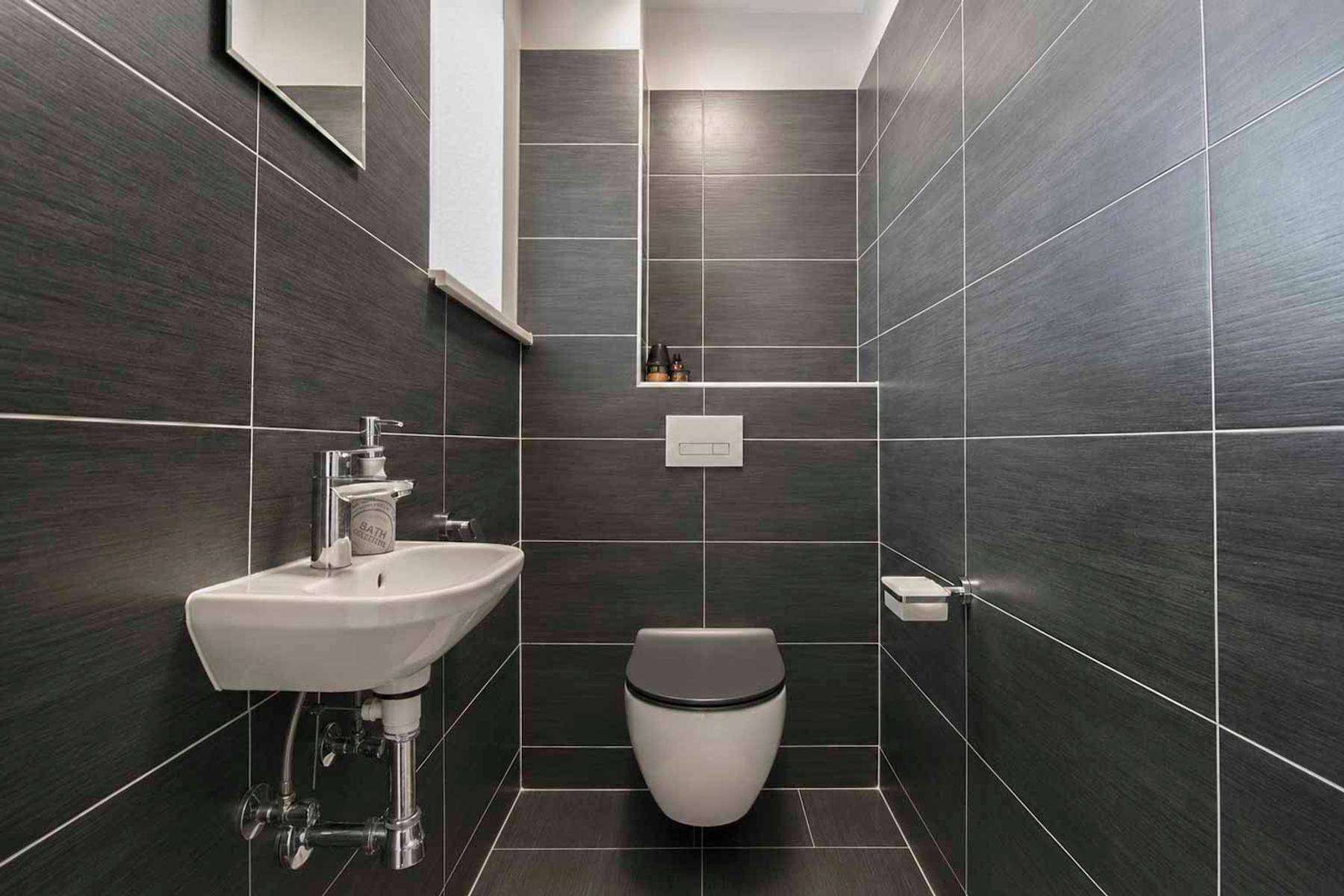 Kleines Gäste-WC mit dunklen Fliesen, wandhängendem WC und modernem Waschbecken.