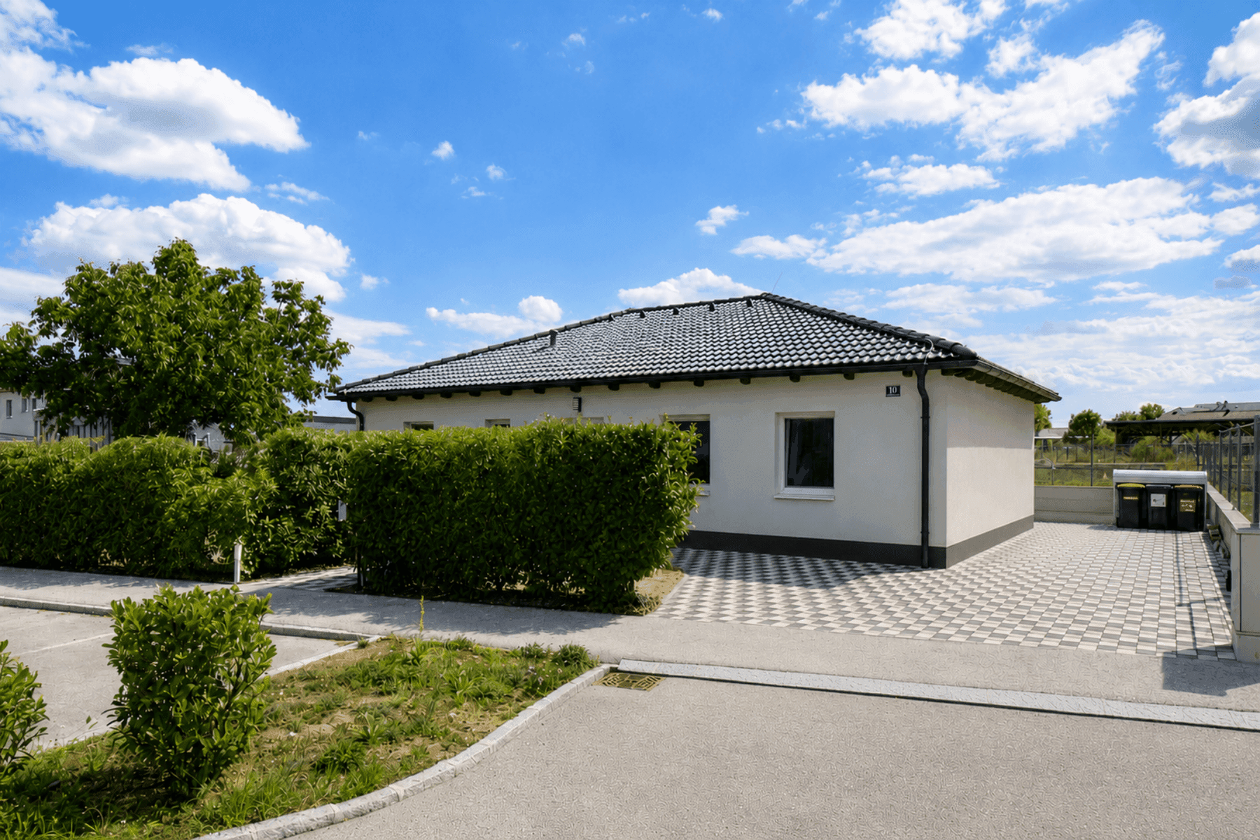 Ansicht des modernen Einfamilienhauses von der Straßenseite mit Parkplätzen und Hecke.