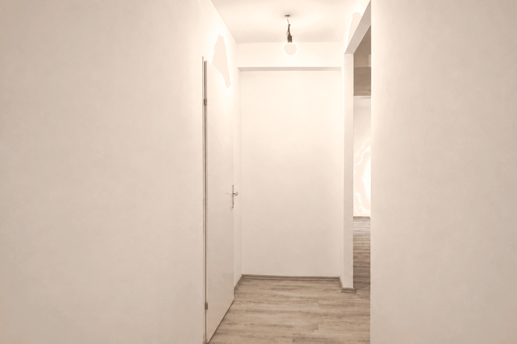 Heller Flur mit Holzboden und einfacher Deckenbeleuchtung, der zu weiteren Räumen führt.