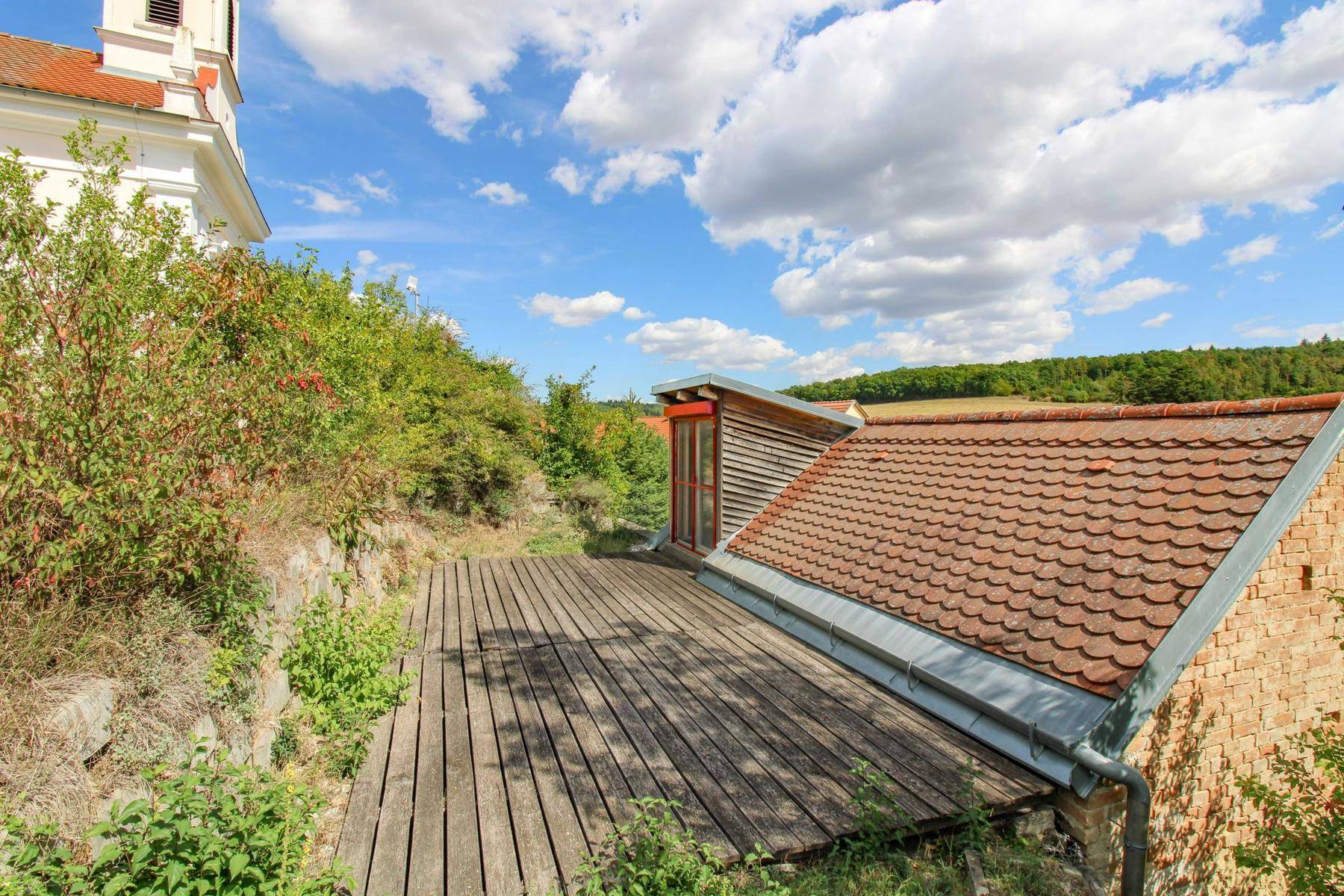 Große Holzterrasse mit Blick auf die Landschaft und angrenzendes Gebäude mit Ziegeldach.