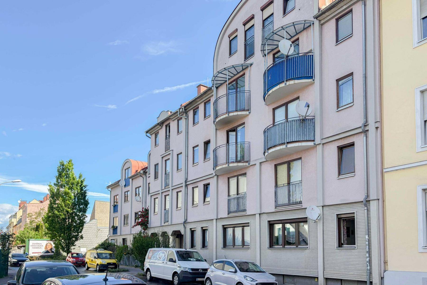Fassade eines Mehrfamilienhauses mit mehreren Balkonen und Satellitenschüsseln an einem sonnigen Tag.
