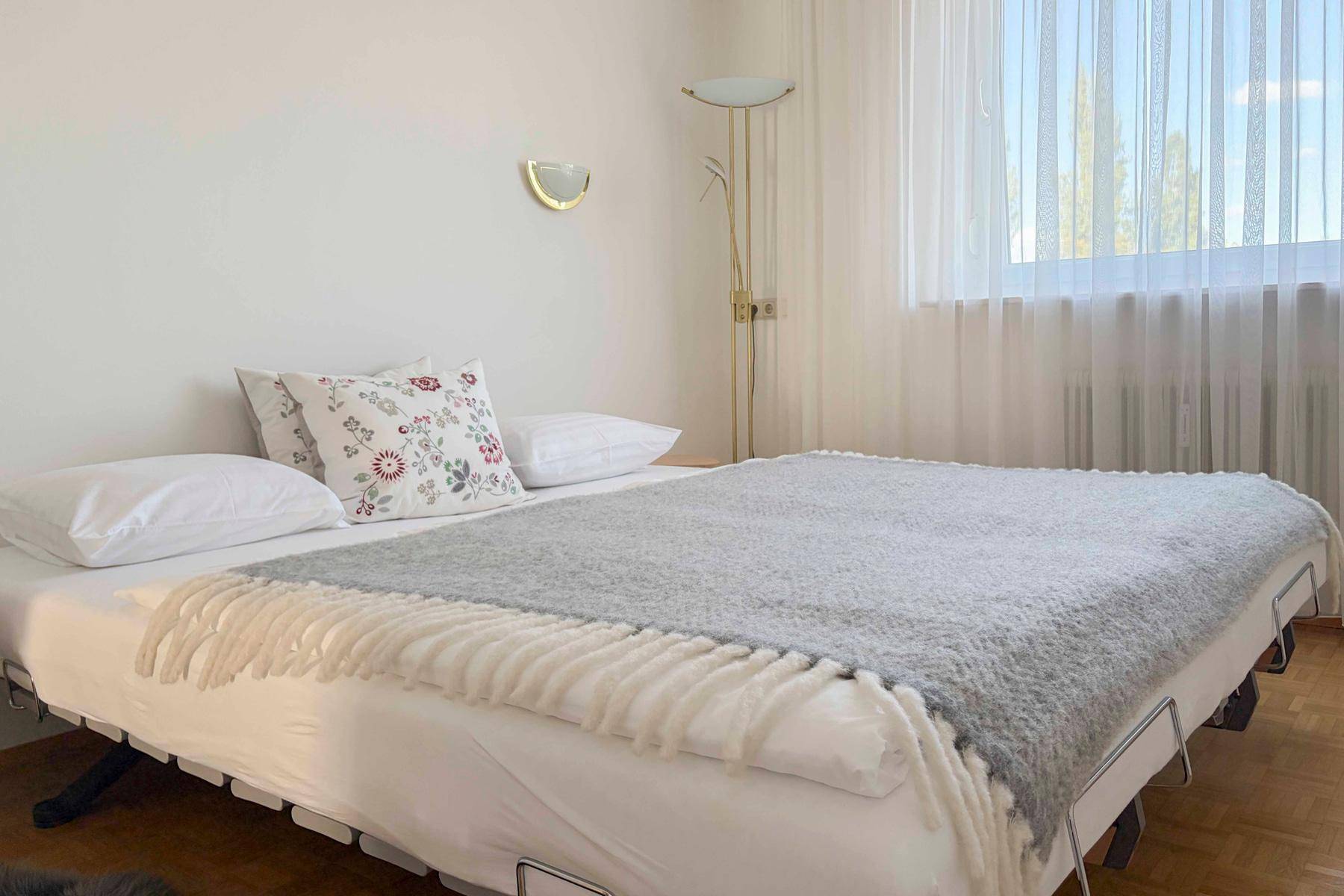 Gemütliches Schlafzimmer mit Doppelbett, Parkettboden und hellem Fenster.