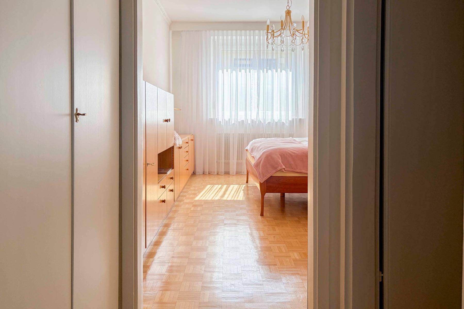 Blick in ein helles Schlafzimmer mit Parkettboden und einem großen Fenster.