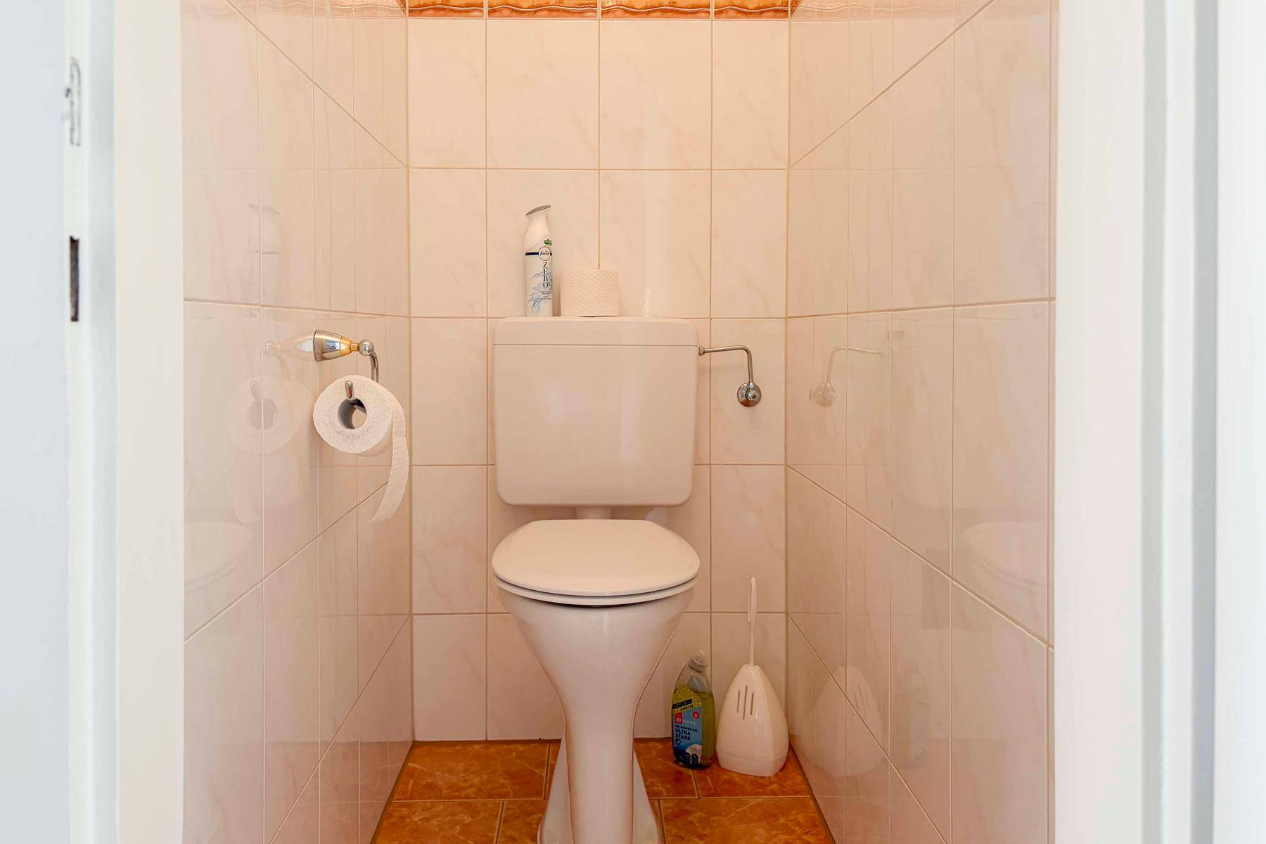 Separates WC mit Toilette und hellen Fliesen an Wänden und Boden.