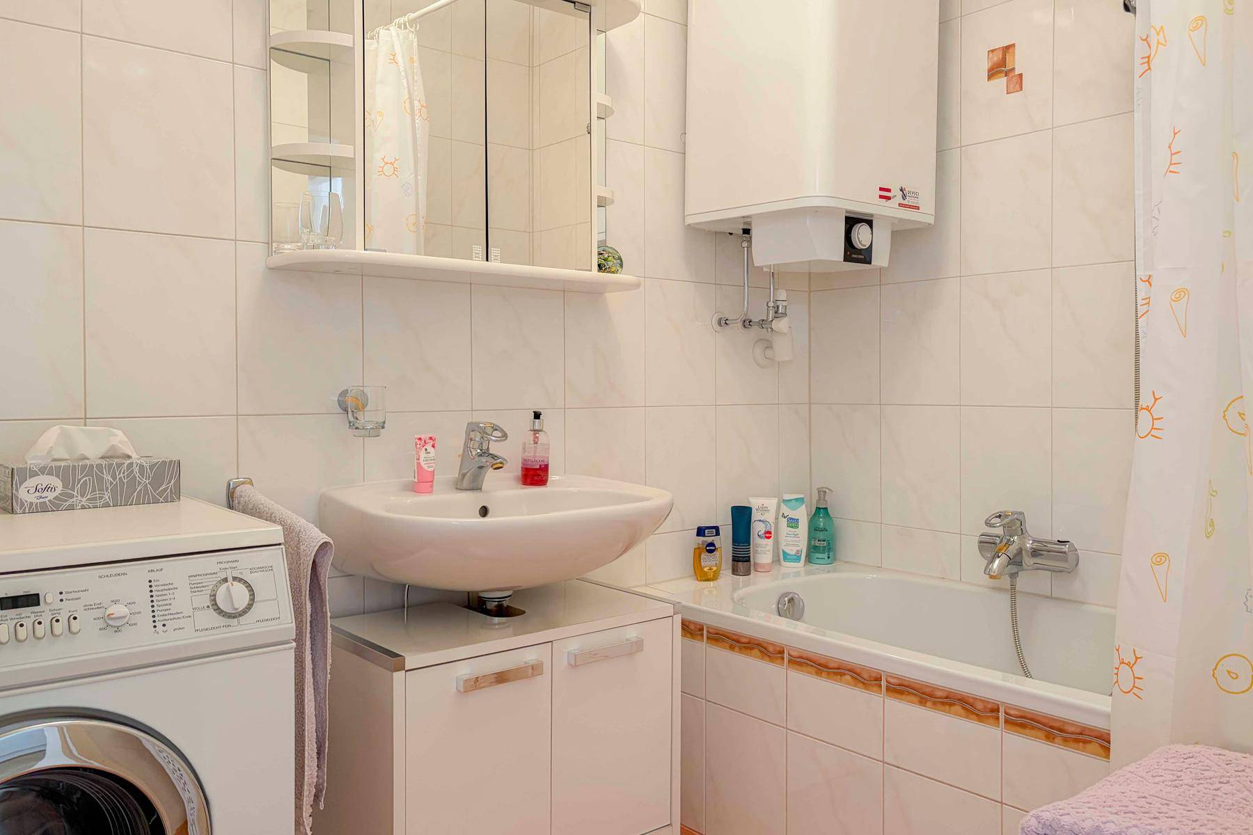 Gefliestes Badezimmer mit Badewanne, Waschbecken und Waschmaschine.