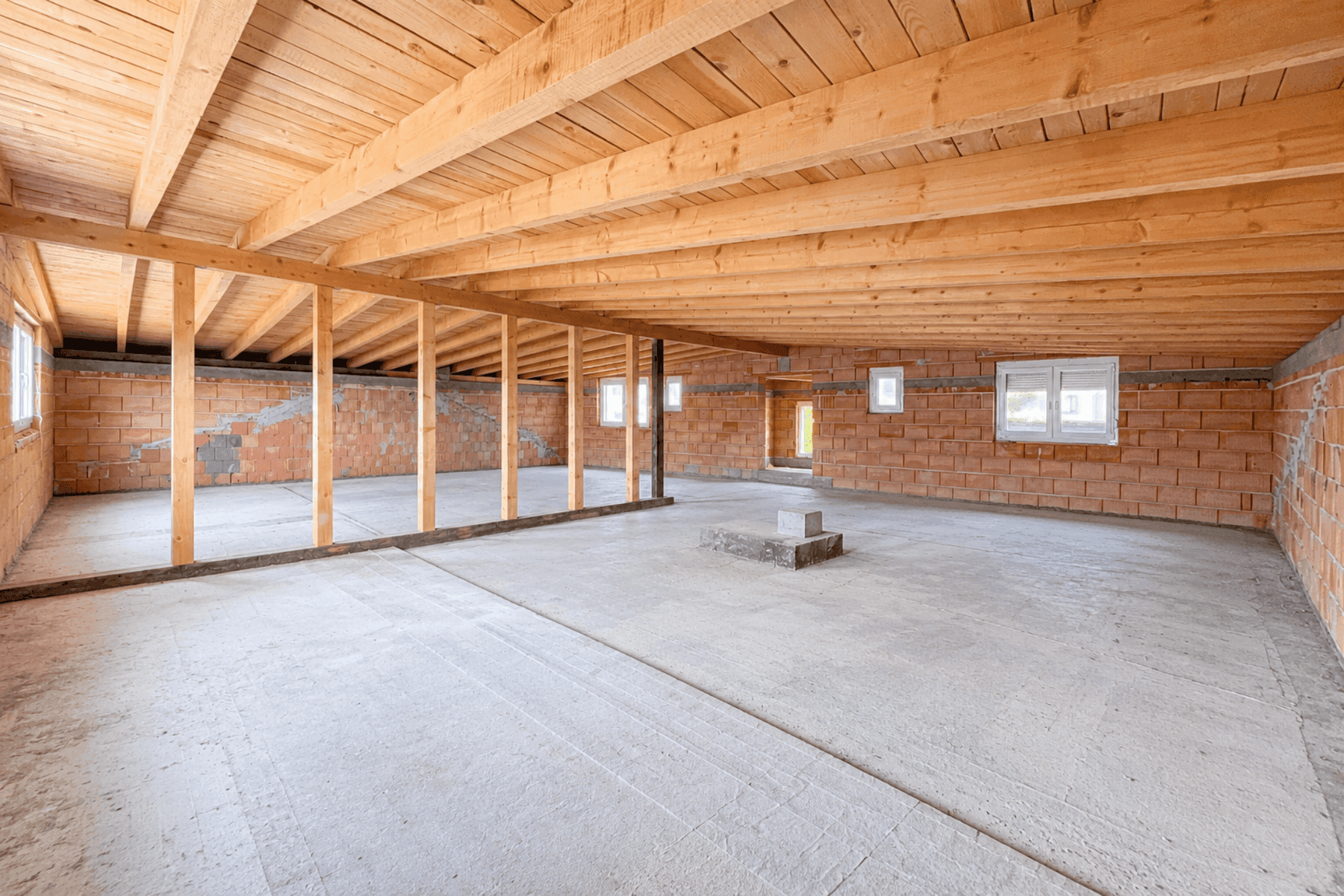 Unfertiger Raum im Untergeschoss mit sichtbaren Holzbalken und Ziegelwänden, bereit für den Ausbau.