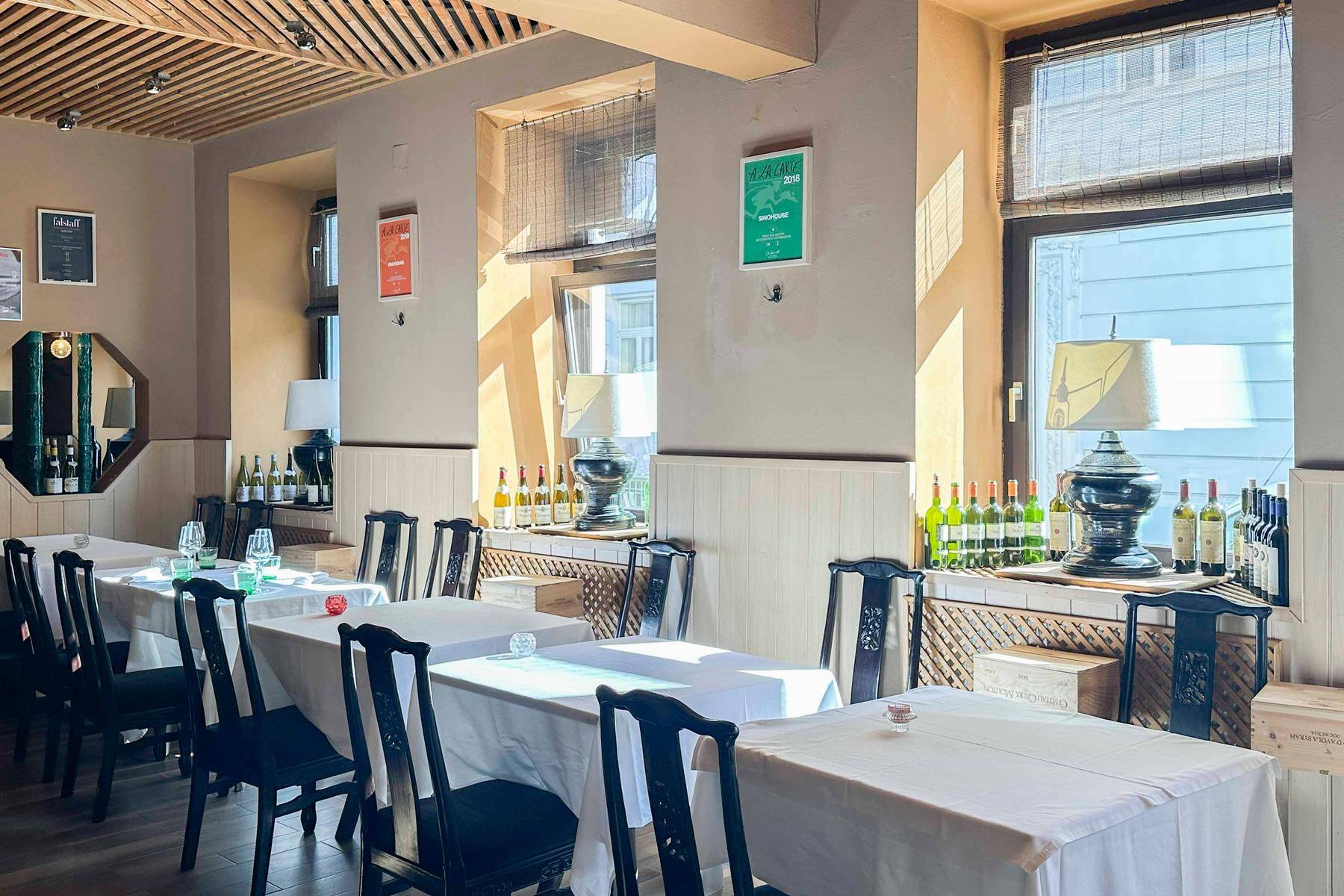 Ein weiterer Blick in den eleganten Restaurant-Speisesaal mit gedeckten Tischen, dunklen Stühlen und hellen Fenstern.