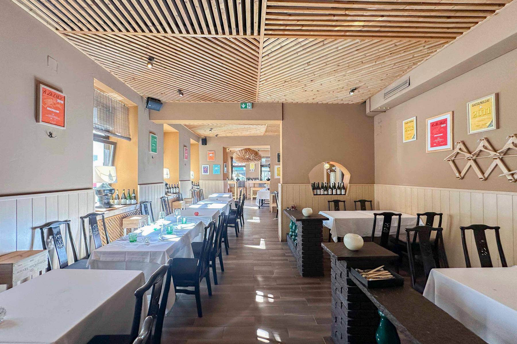 Weitläufiger Restaurantbereich mit einer markanten Holzlamellendecke, vielen Tischen und dekorativen Wandelementen.