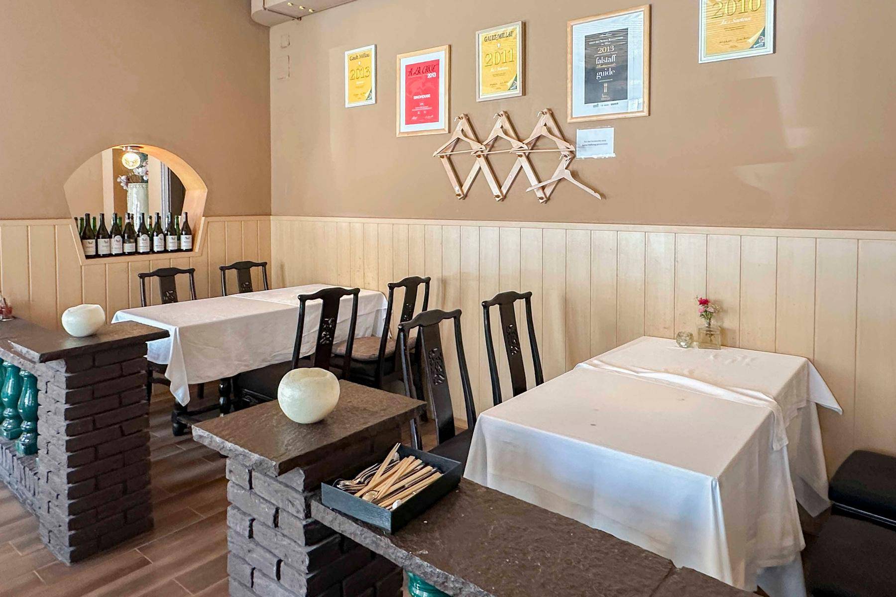 Restaurant-Speisesaal mit gedeckten Tischen, dunklen Stühlen und dekorativen gemauerten Elementen im Vordergrund.