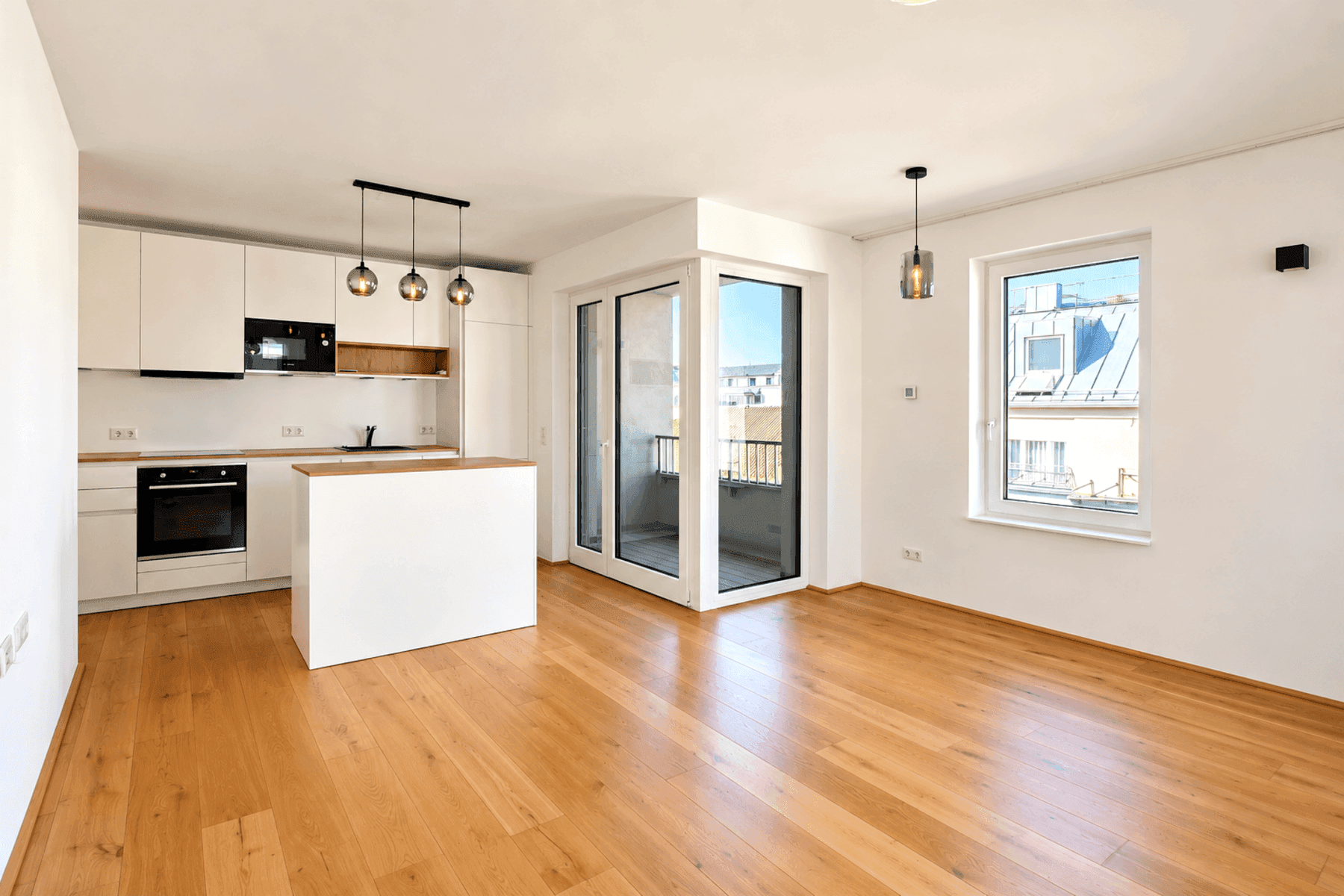 Offener Wohnbereich mit integrierter, moderner Küche, Holzboden und Zugang zu einem Balkon.