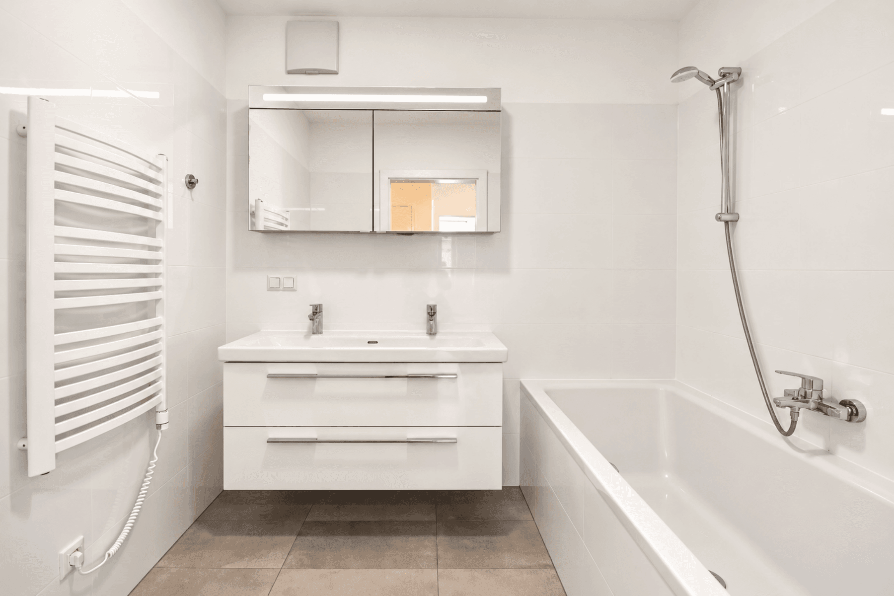 Modernes Badezimmer mit Doppelwaschbecken, Badewanne mit Duschfunktion und weiß gefliesten Wänden.