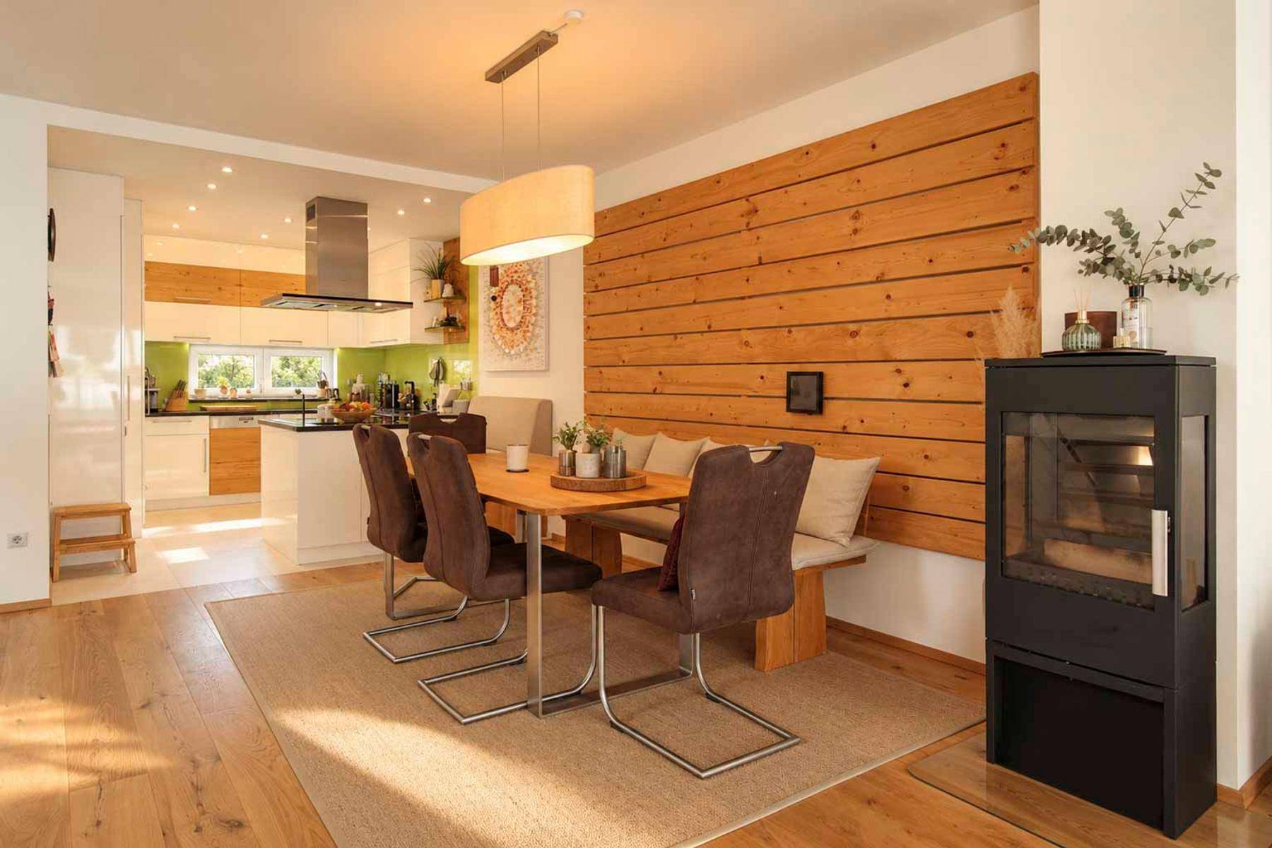 Heller Essbereich mit Holztisch und Sitzbank, Kaminofen und Blick in die moderne Küche.
