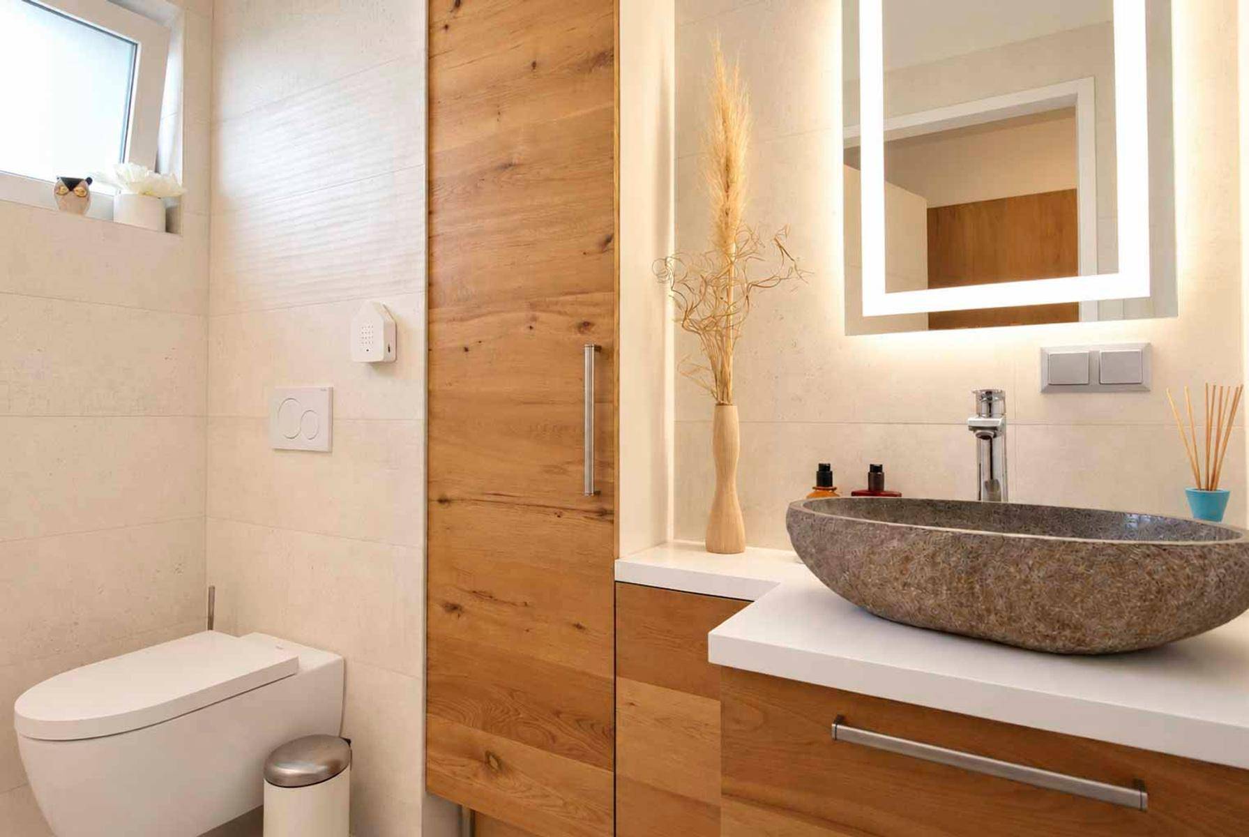 Modernes Gäste-WC mit Natursteinwaschbecken, Holzschrank und beleuchtetem Spiegel.