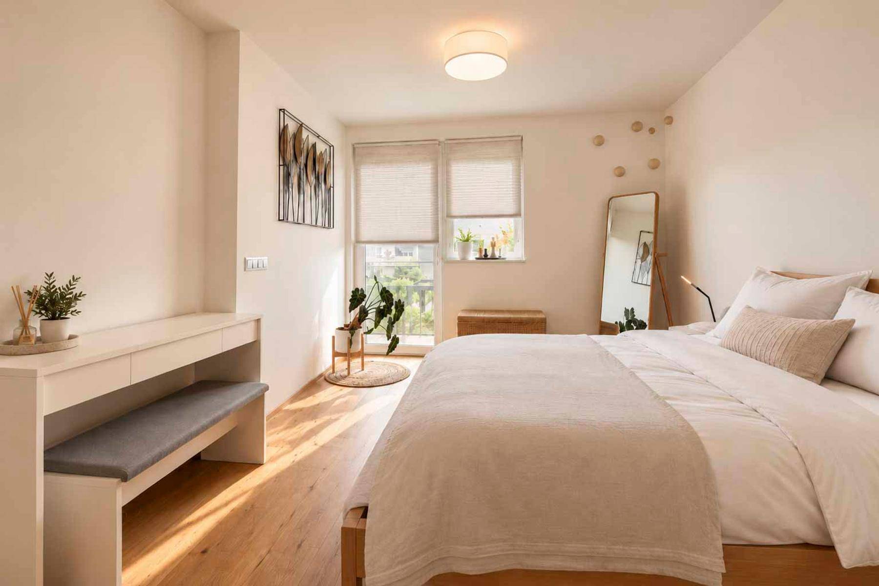 Helles Schlafzimmer mit Holzboden, minimalistischer Einrichtung und Zugang zu einem Balkon.