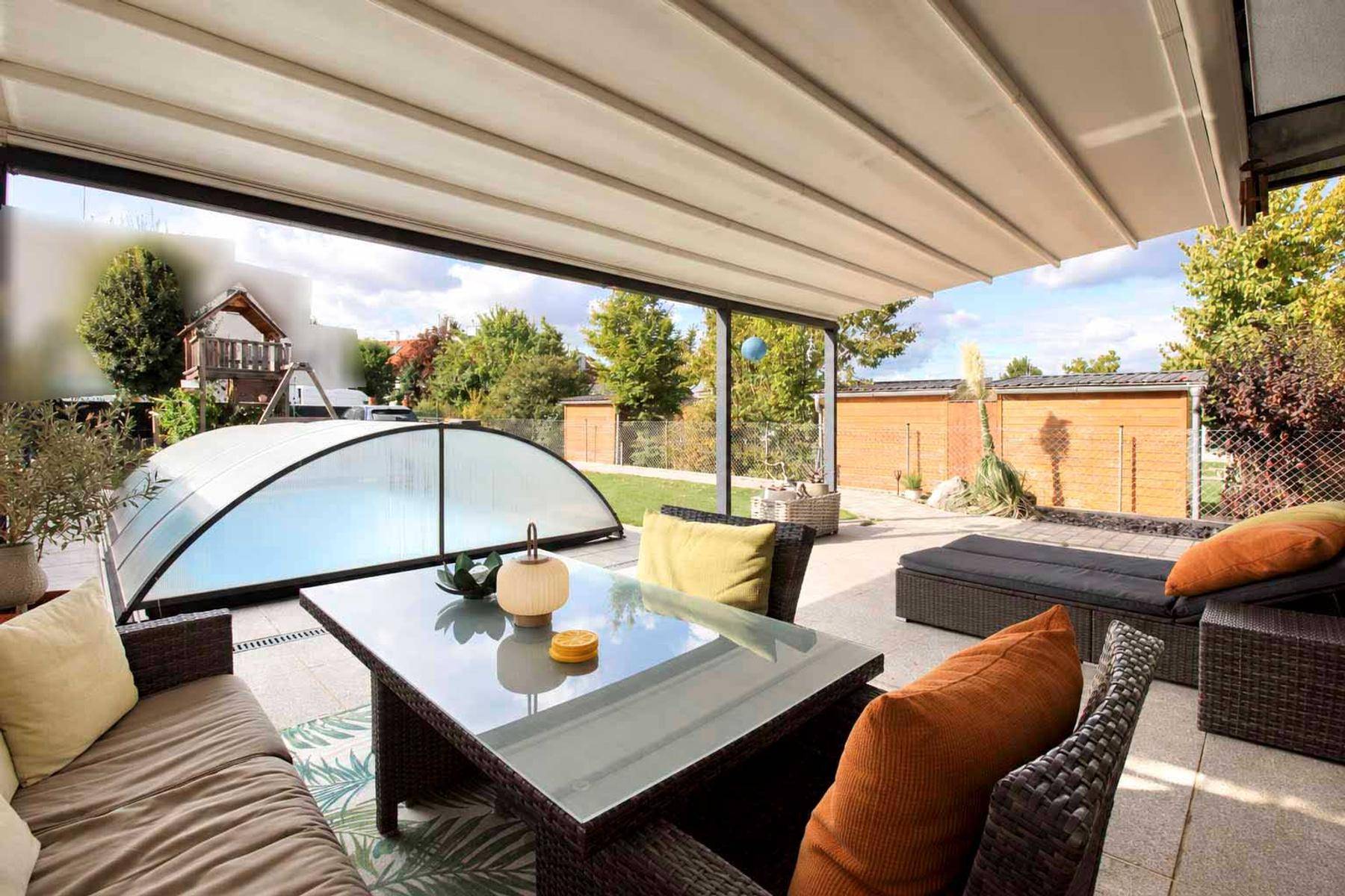 Gemütlicher Sitzbereich auf der Terrasse unter einer ausfahrbaren Markise mit Blick auf den Pool.