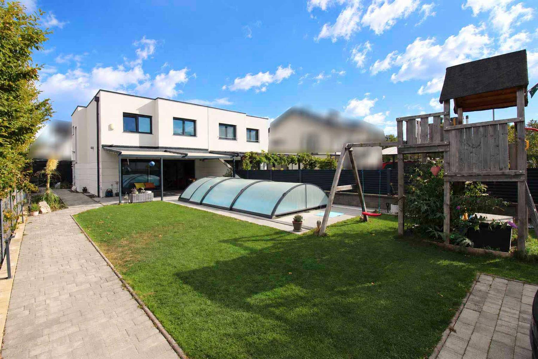 Großer Garten mit Rasenfläche, Spielplatz und überdachtem Pool hinter einem modernen Haus.