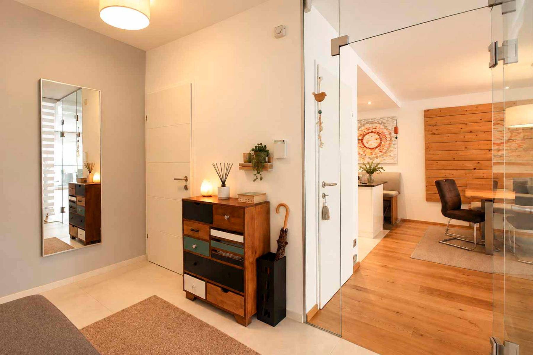 Heller Eingangsbereich mit Garderobe, Spiegel und Glaswand zum Wohnbereich.