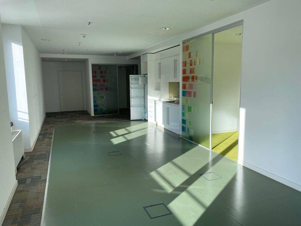 Heller Bürobereich mit integrierter Küchenzeile und farbigen Glaswänden, die den Raum strukturieren.