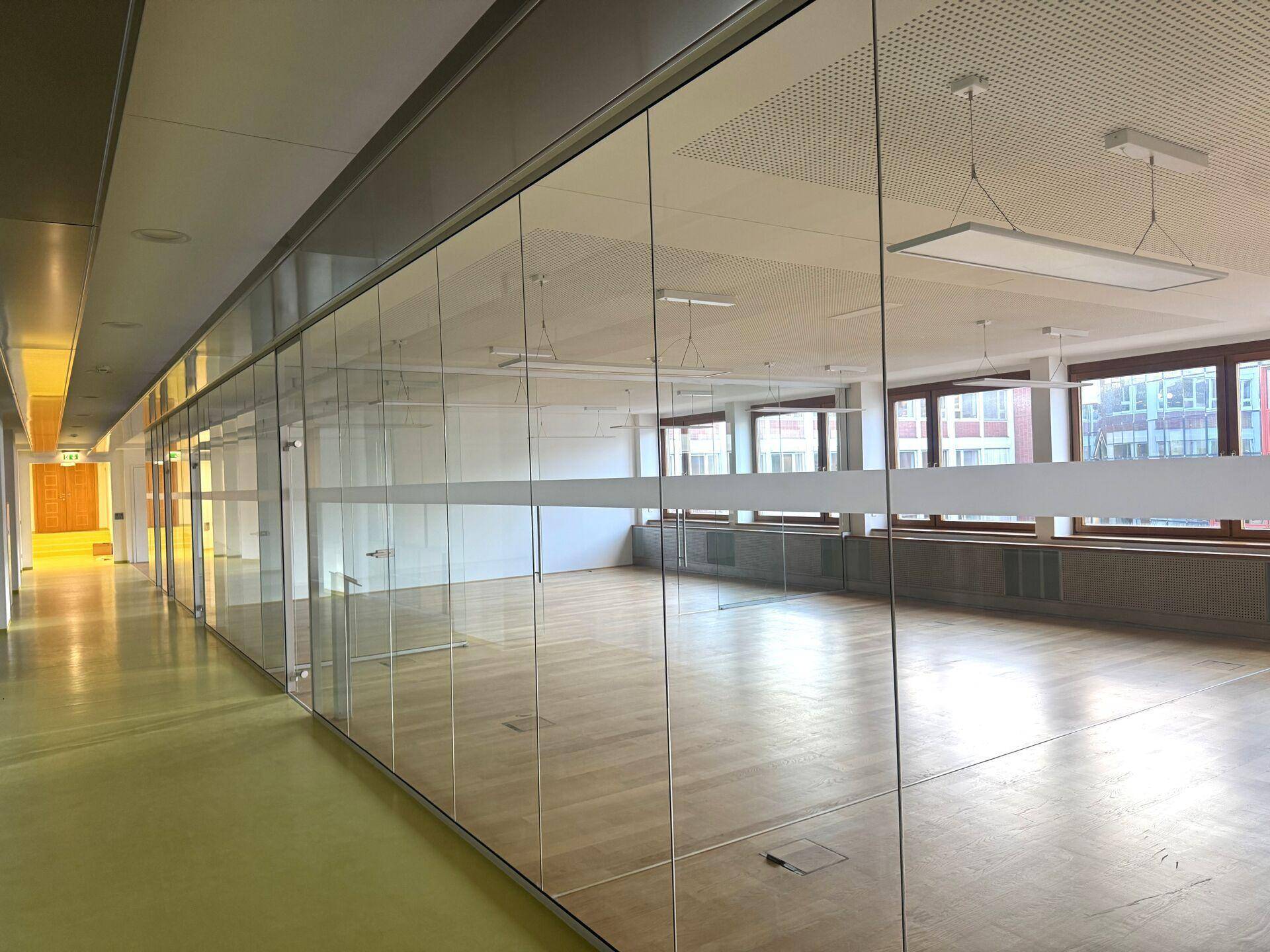 Modernes Büro mit Glaswänden, Holzboden und viel Tageslicht, ideal für eine offene Arbeitsumgebung.