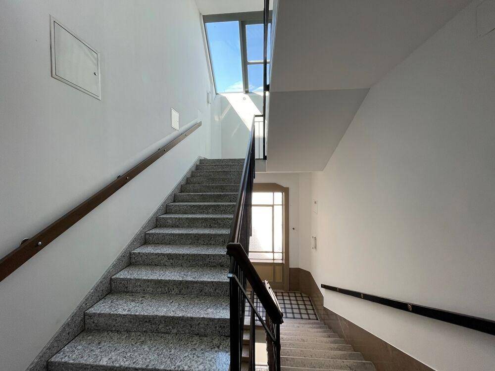 Helles Treppenhaus mit Granitstufen, Holzgeländer und Fenstern, die natürliches Licht spenden.