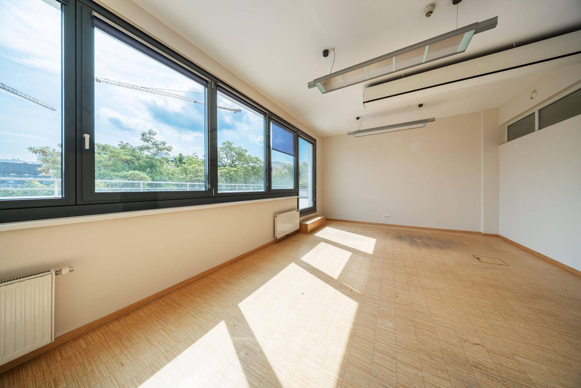 Geräumiger Büroraum mit großen Fenstern, viel Tageslicht und Holzboden.